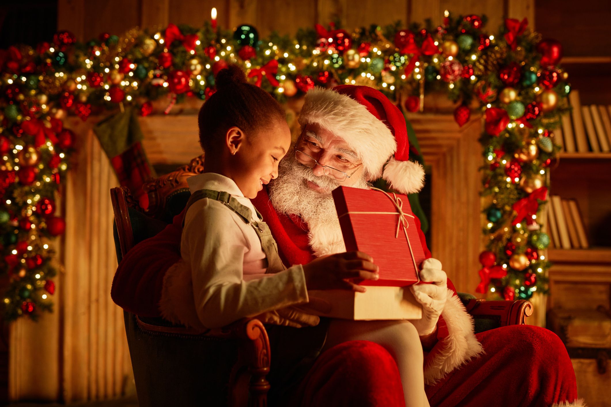 A child sits on Santa’s lap, smiling as they open a red gift box, surrounded by festive decorations, garlands, and warm lighting, capturing Christmas in Devon magic.