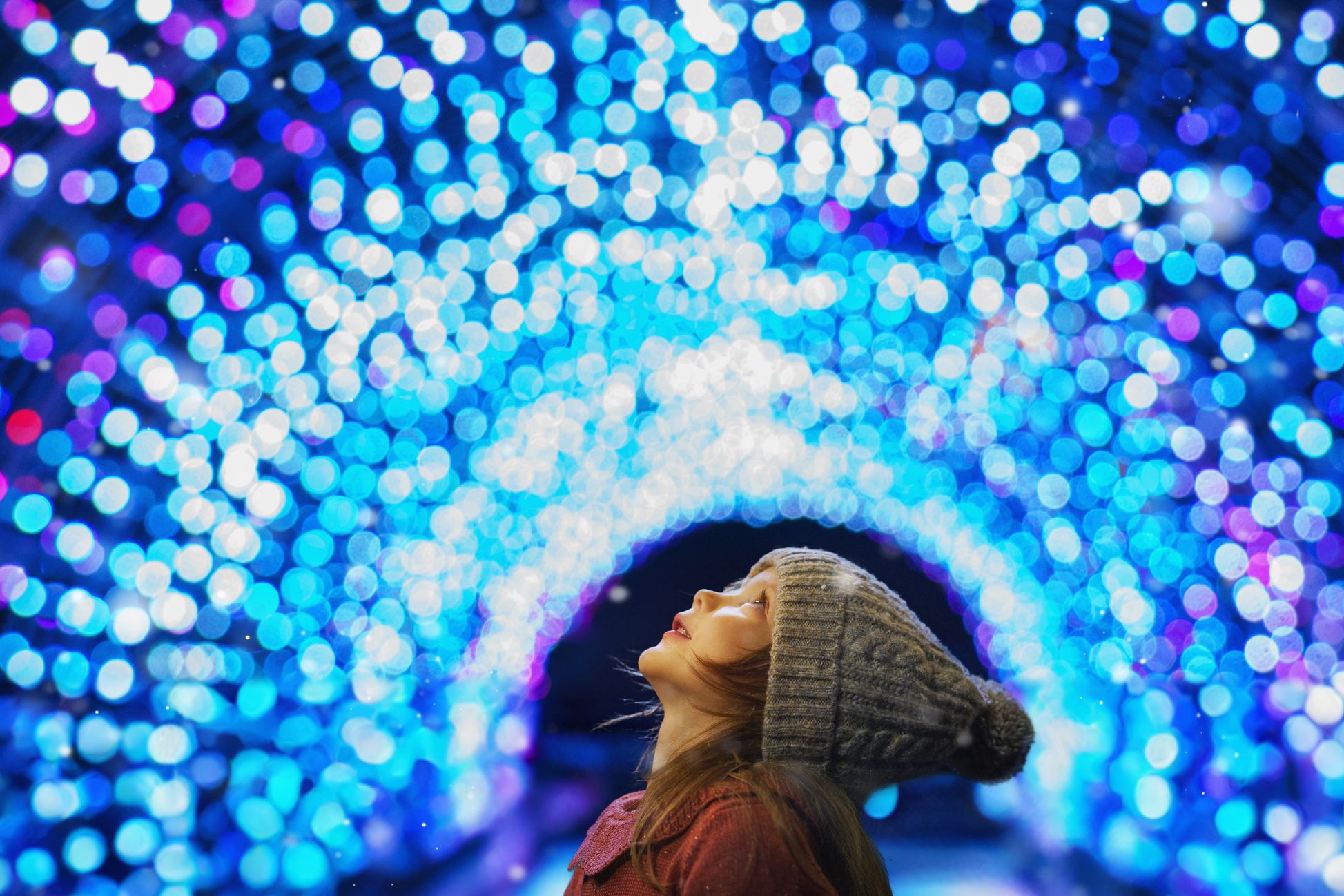 A child in a knit hat gazes upward in awe beneath a canopy of vibrant blue and purple lights, capturing the festive magic of Christmas in Devon.