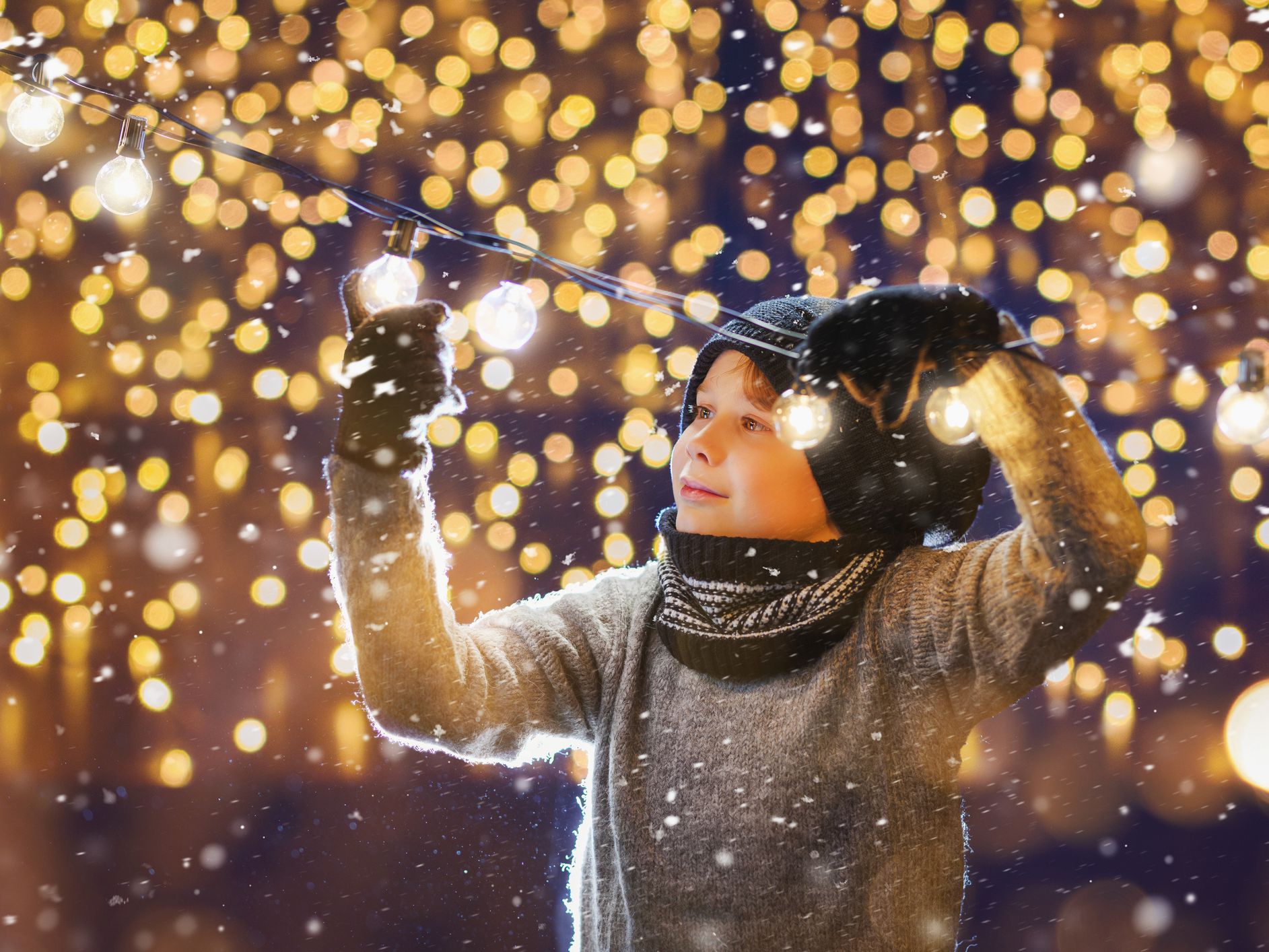 A child in warm winter clothing admires string lights in a snowy scene, surrounded by a golden bokeh background, encapsulating the festive spirit of Christmas in Devon.