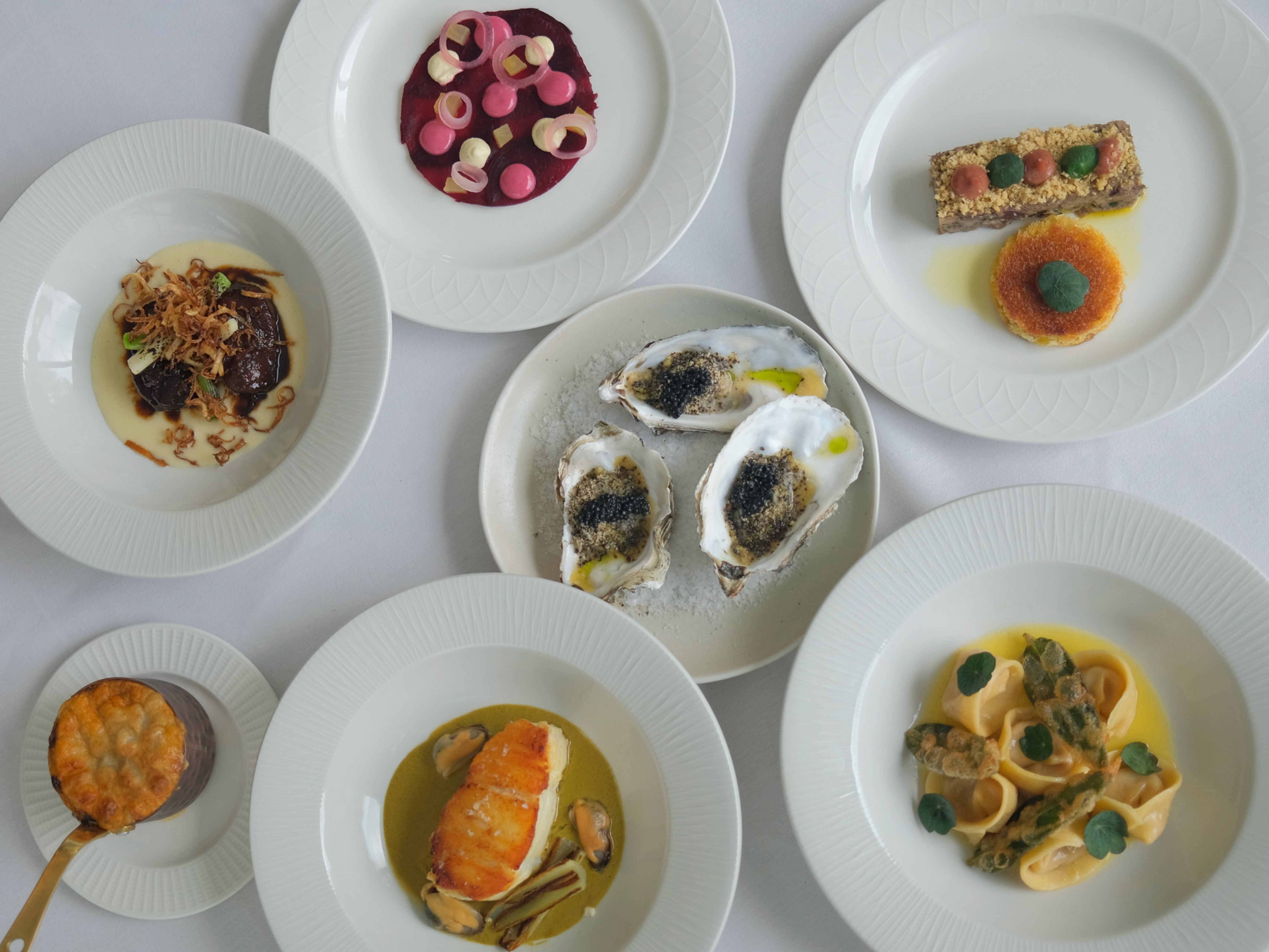 An assortment of gourmet dishes served on white plates, artistically arranged on a white tablecloth.