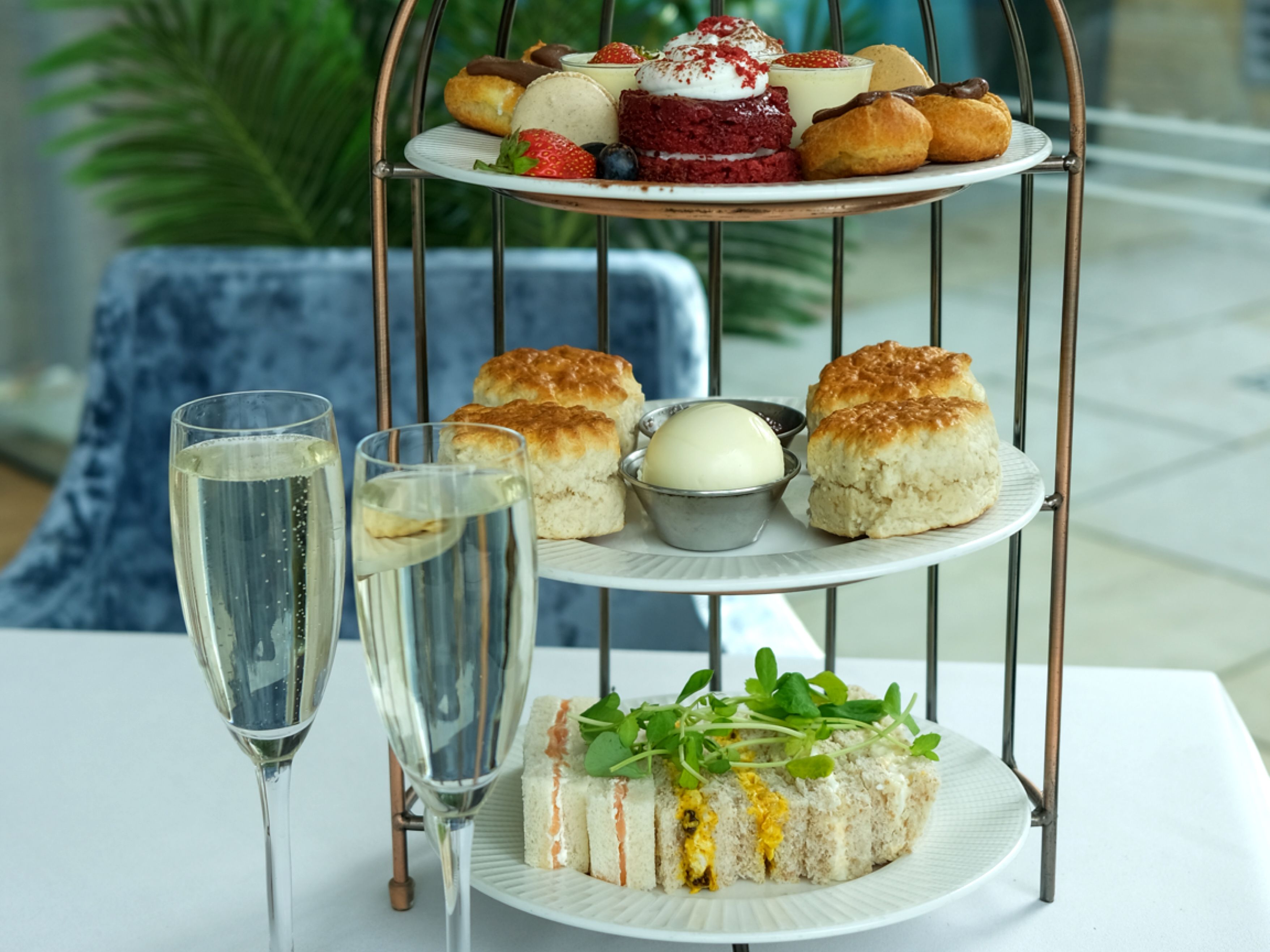Afternoon tea set with sandwiches, scones, pastries, and two glasses of champagne on a white tablecloth.