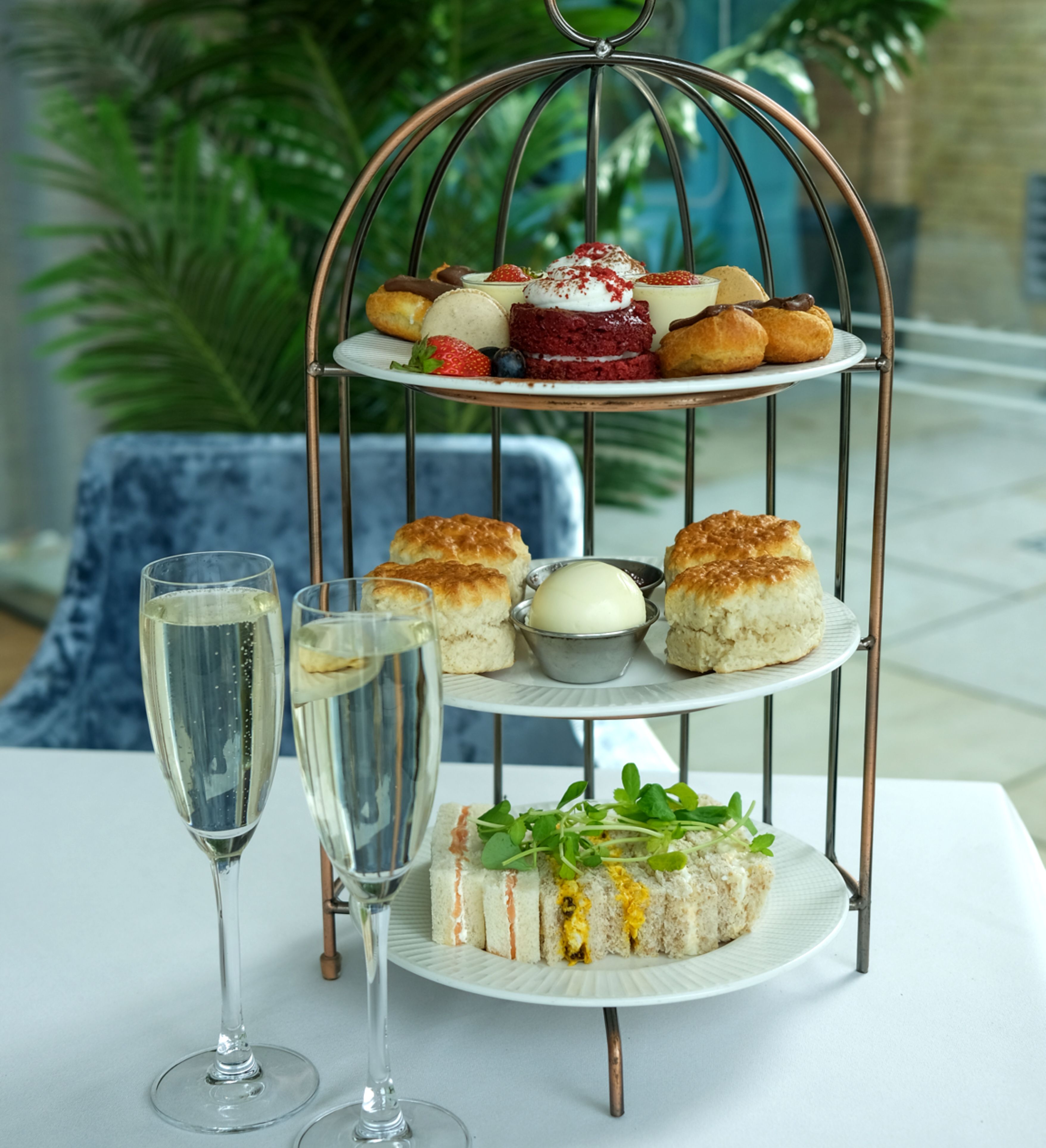 Afternoon tea set with sandwiches, scones, pastries, and two glasses of champagne on a white tablecloth.