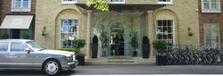 Entrance of a modern boutique hotel with glass doors, a classic car parked in front, and a row of bicycles to the side.