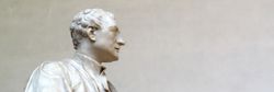 Marble statue of Sir Isaac Newton in academic robes, holding a book, shown in profile against a plain background.