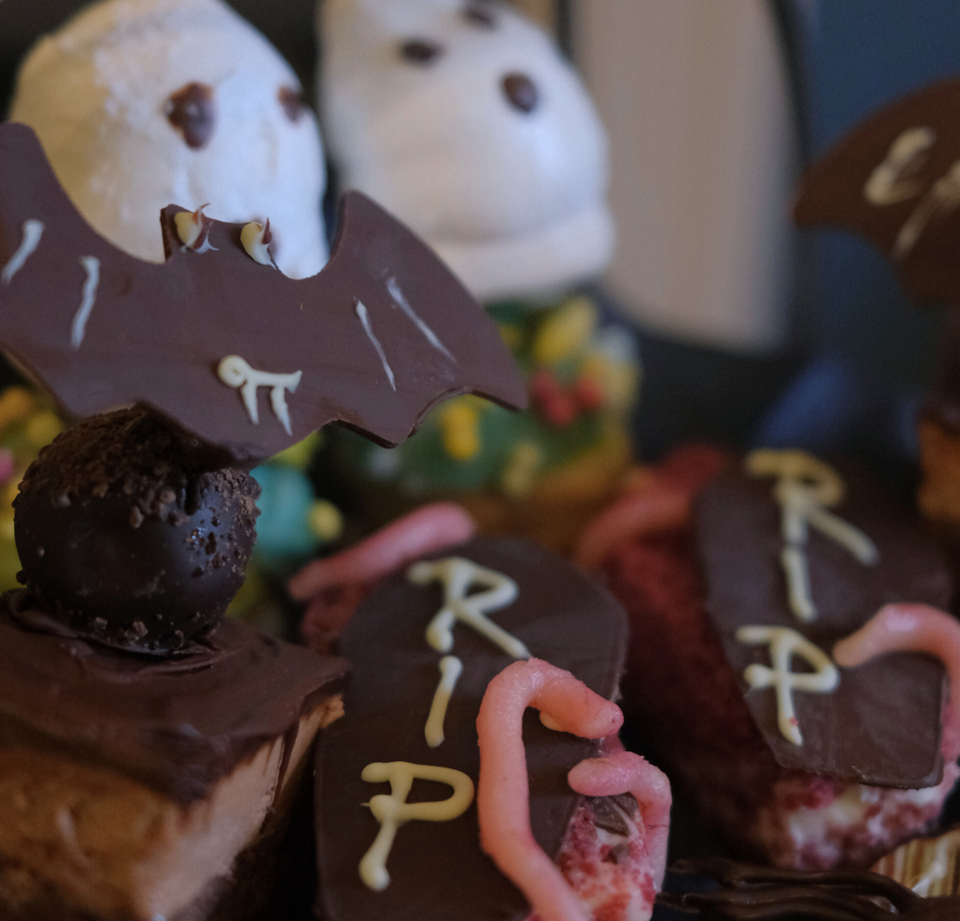 Halloween-themed desserts with chocolate bats, tombstone decorations with 'RIP', and ghost-shaped treats