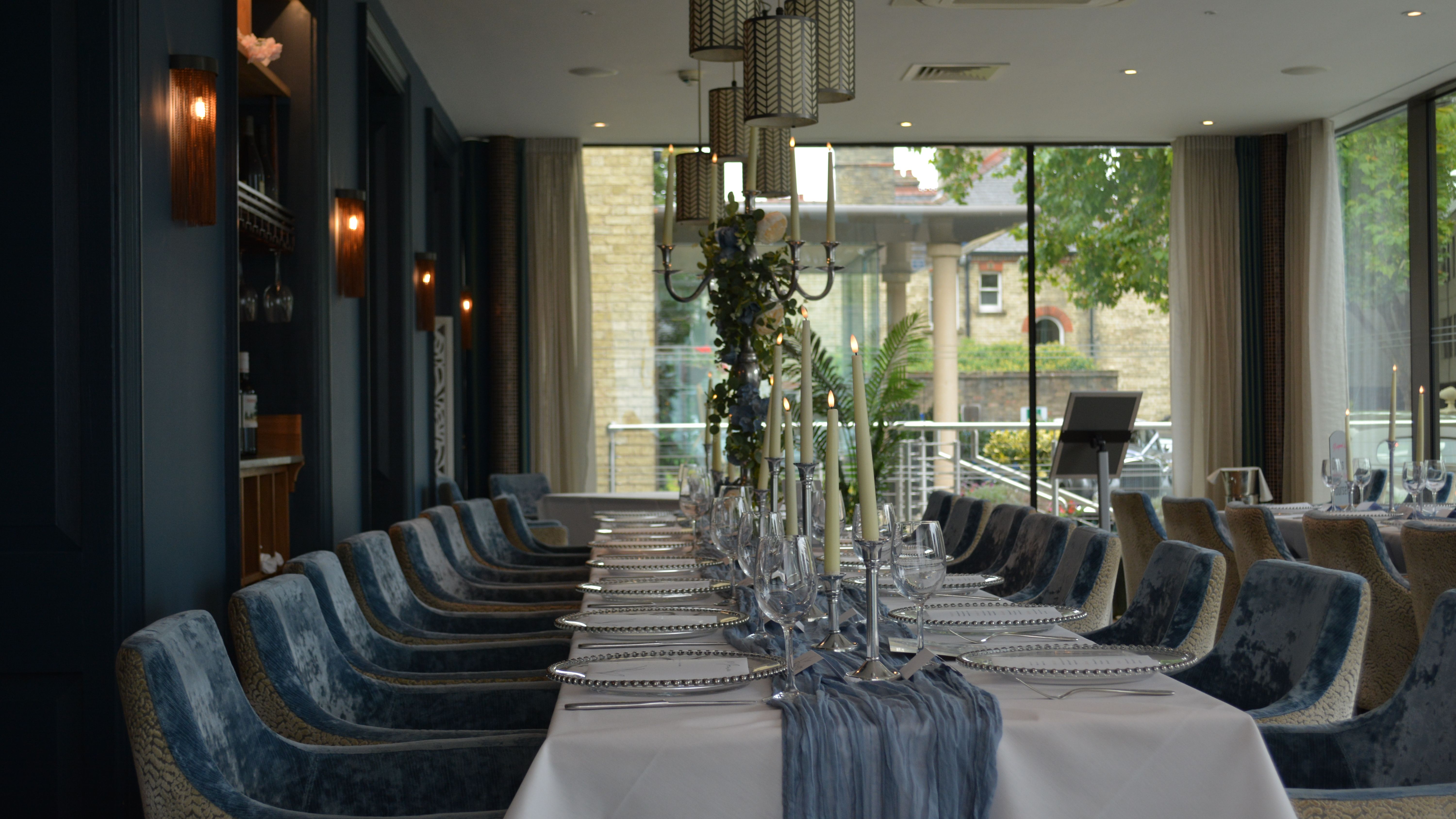 Elegant dining table set for a formal event in a stylish restaurant with velvet chairs and candles.