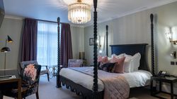 A stylish hotel room with a four-poster bed, elegant lighting, and floral accent decor.