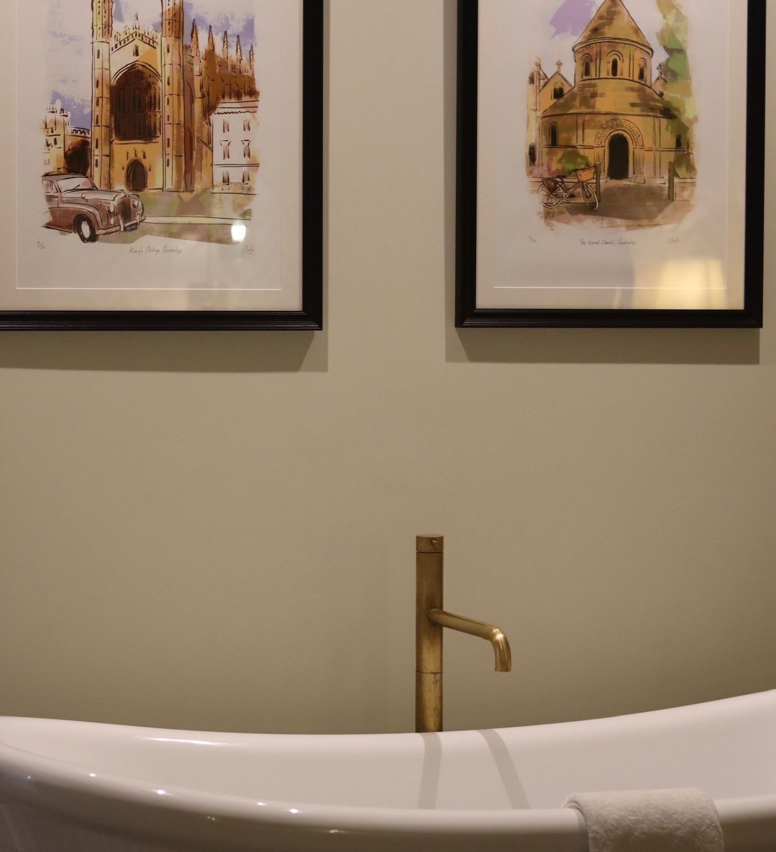 Freestanding bathtub with golden faucet and two framed architectural artworks hanging above it
