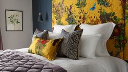 A stylish bed with white linens, decorative pillows, and a vibrant yellow floral headboard