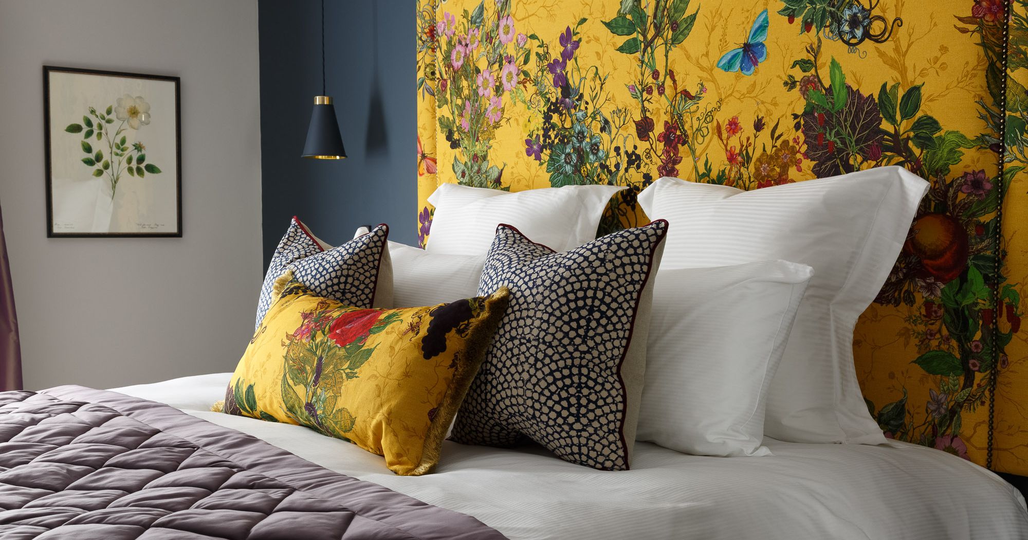 A stylish bed with white linens, decorative pillows, and a vibrant yellow floral headboard