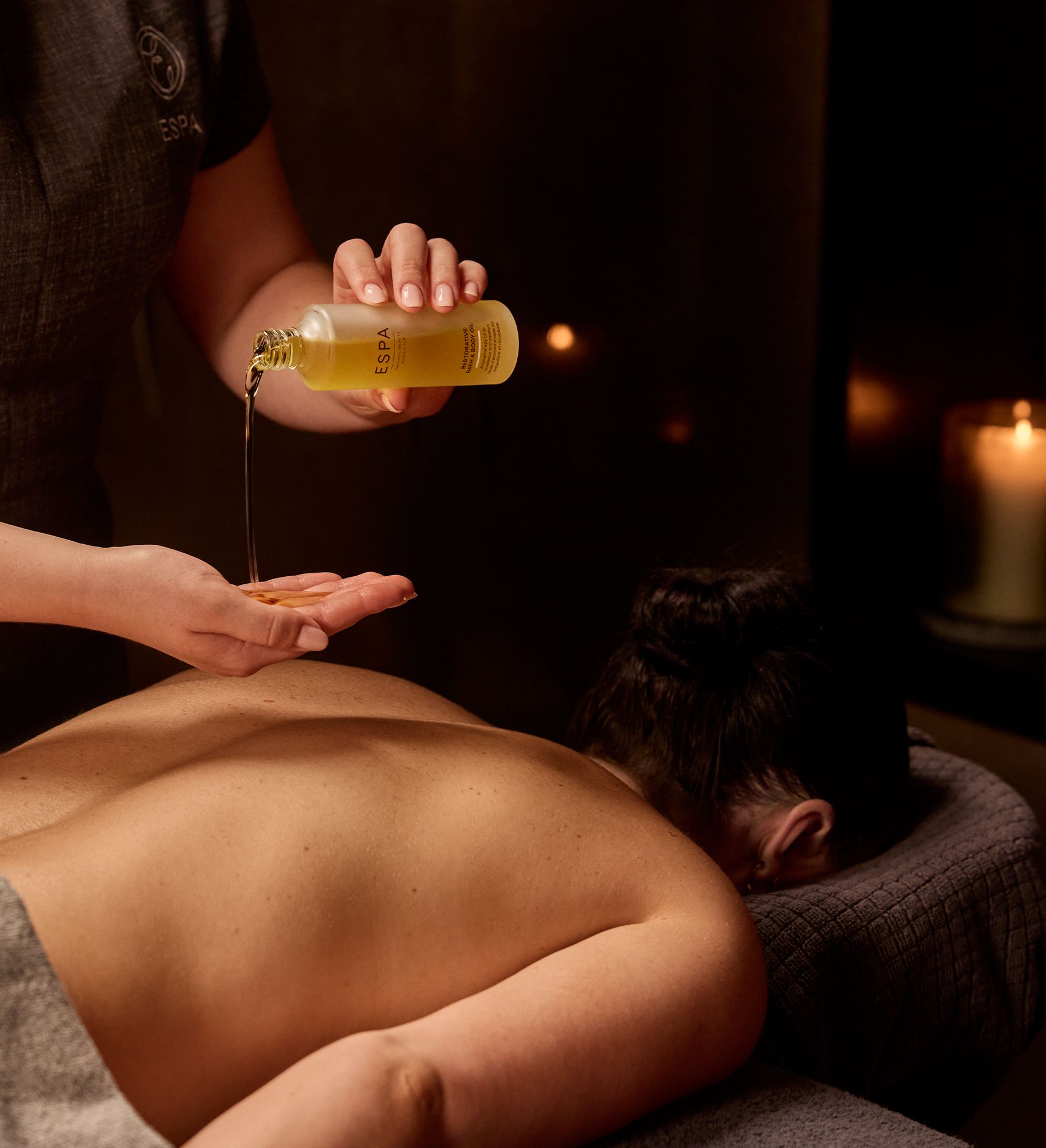 A person receives a back massage while aromatic oil is poured onto the hands of a massage therapist.