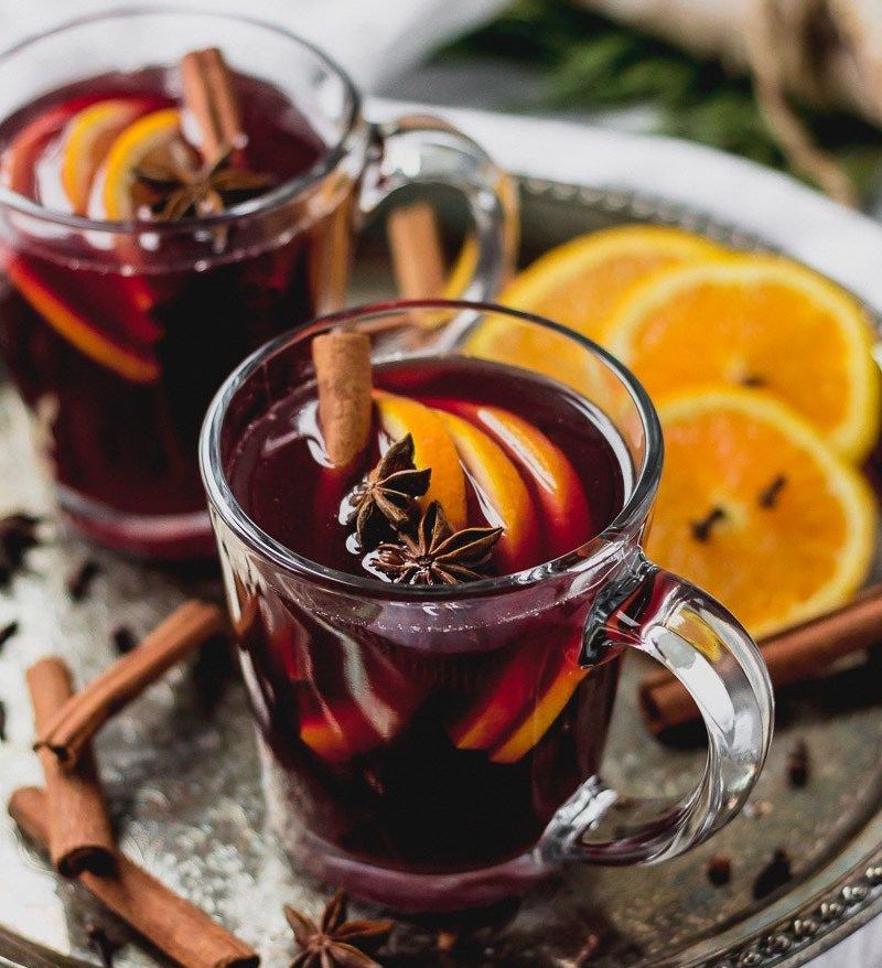 Two glass mugs of mulled wine garnished with orange slices, cinnamon sticks, and star anise on a decorative tray.