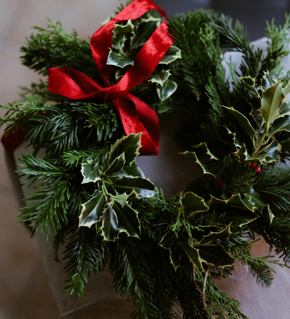 Christmas wreath made of evergreen branches, holly leaves, and a red velvet bow