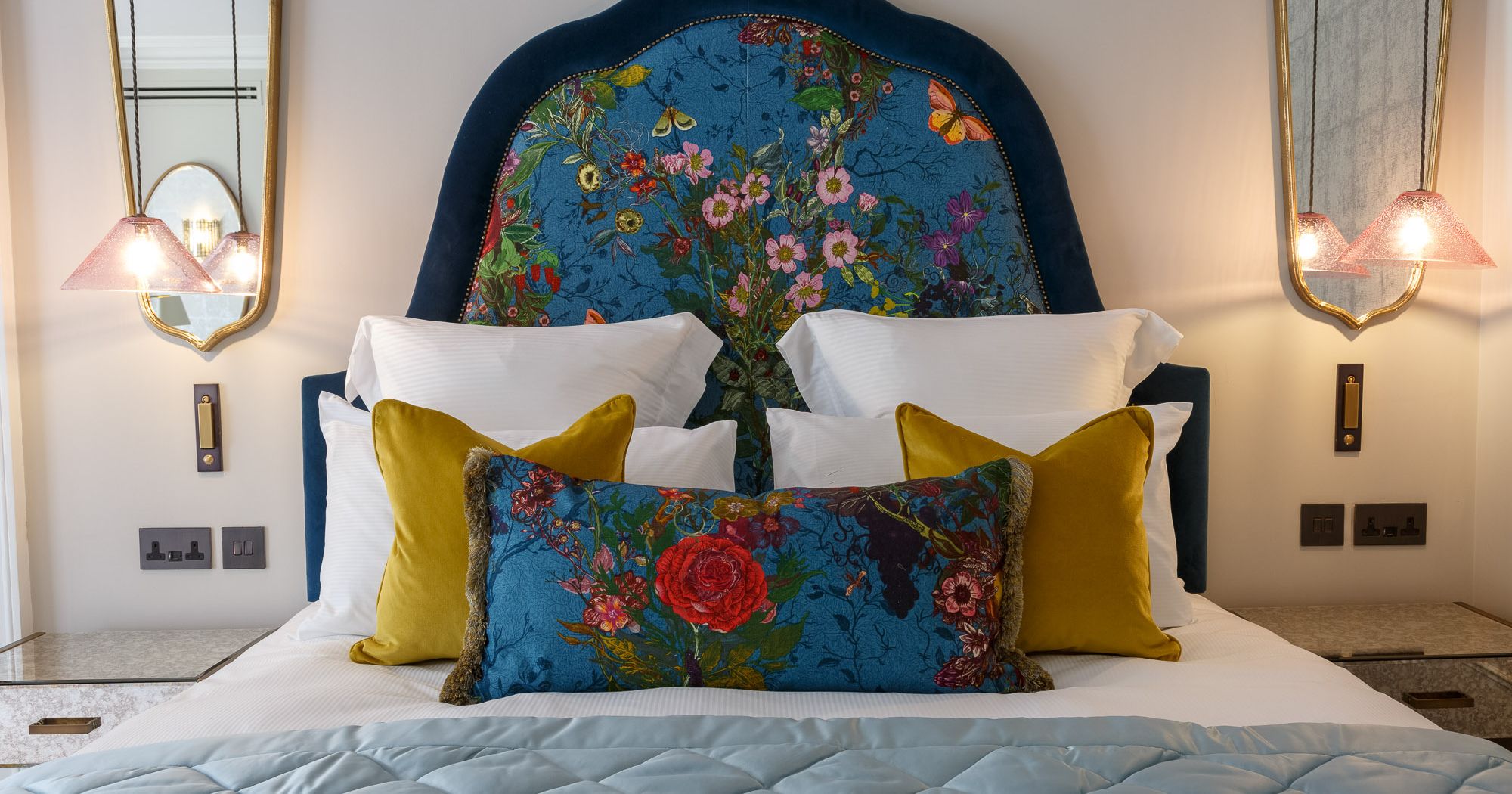 A stylish bed with a blue floral headboard, colorful pillows, and modern bedside lighting.