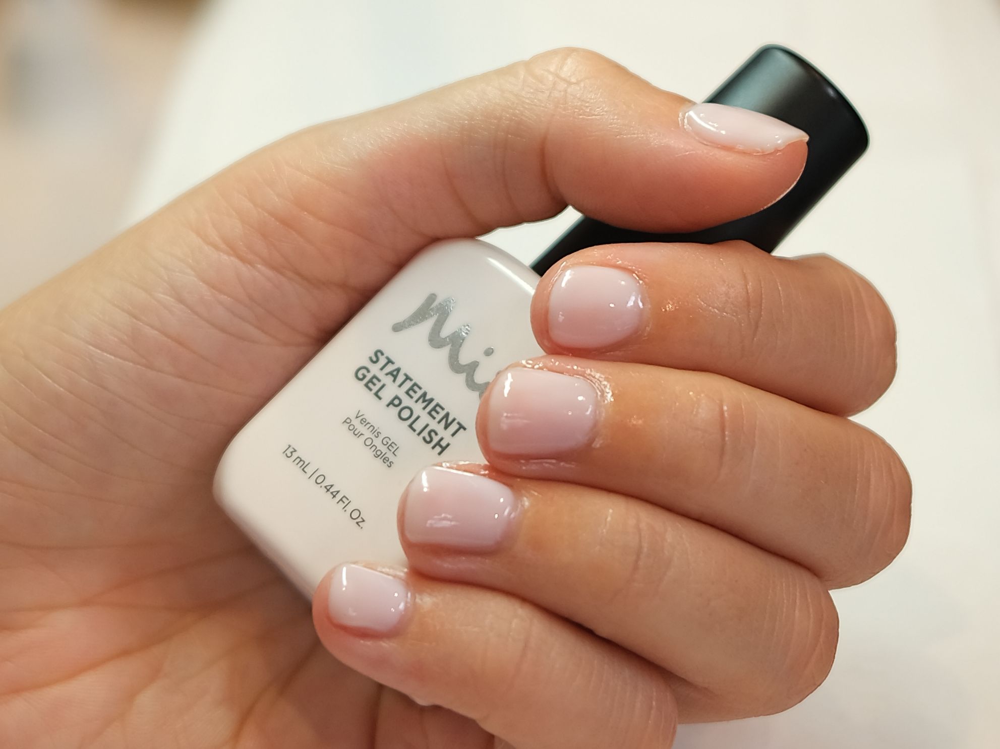 Hand holding a bottle of gel nail polish with freshly manicured nails