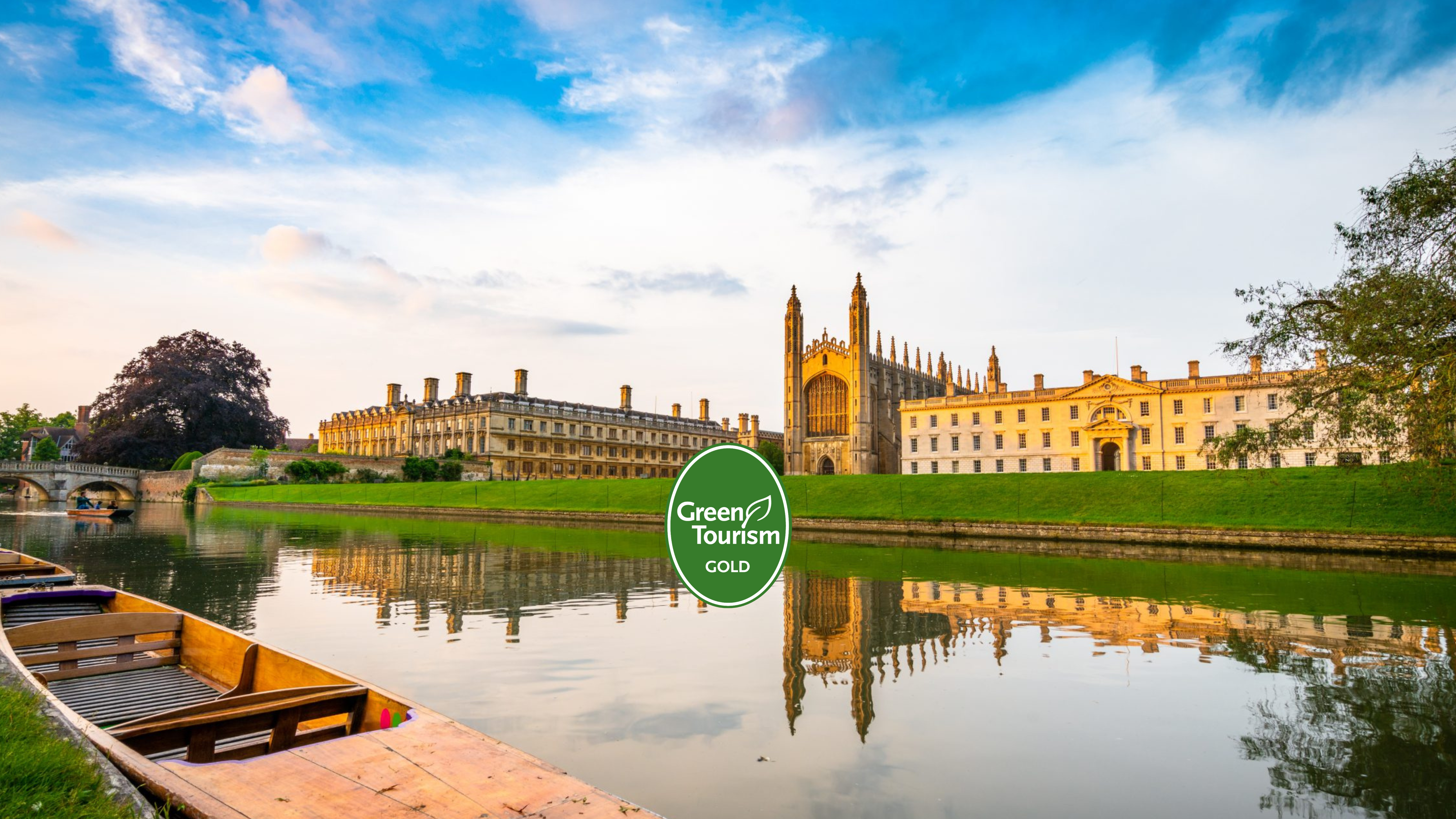 Scenic view of Cambridge University's King's College Chapel, river, and punts under a blue sky with a Green Tourism Gold badge in the center.