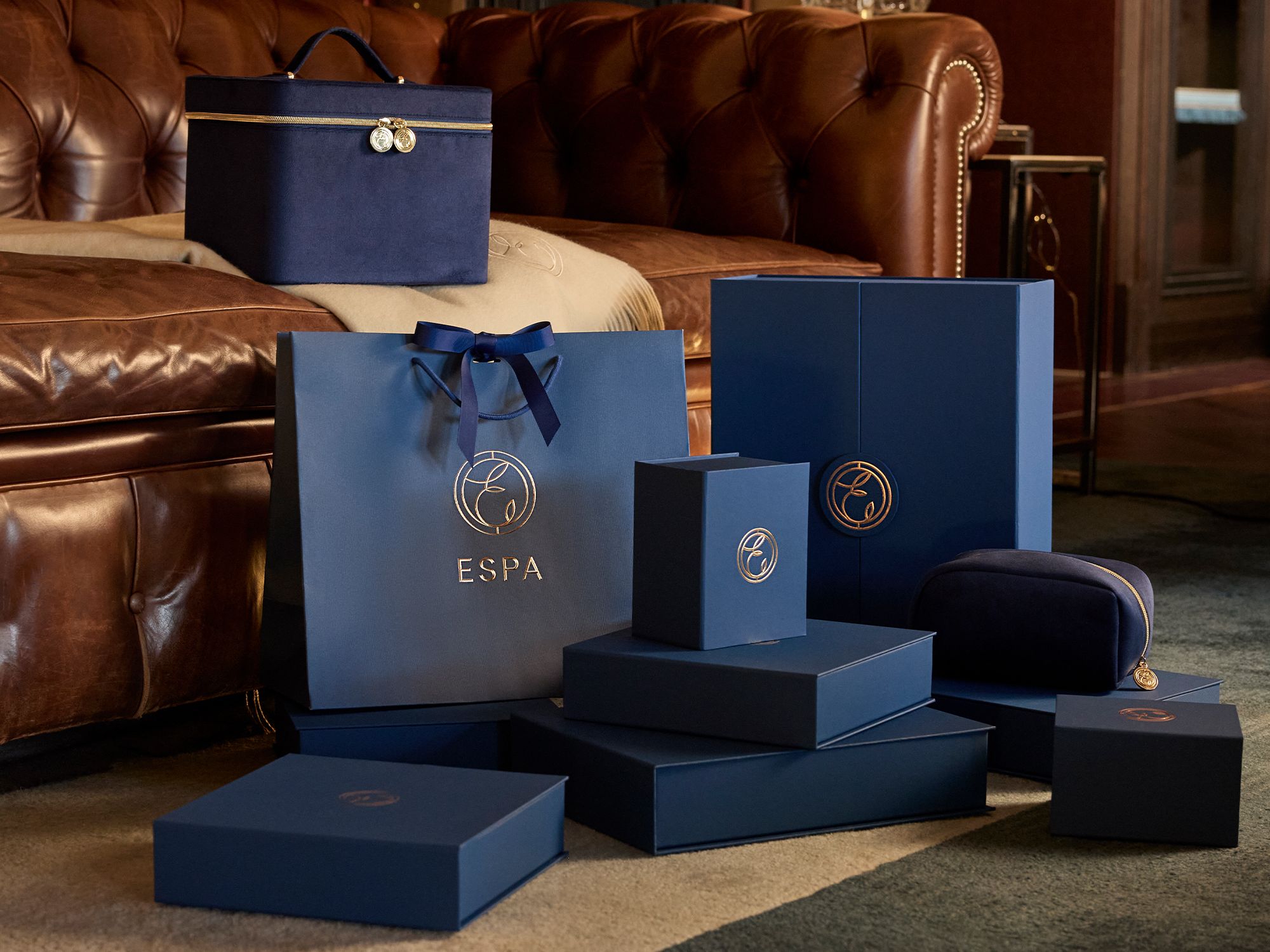 Luxury ESPA gift boxes and bags in dark blue arranged in front of a brown leather sofa.