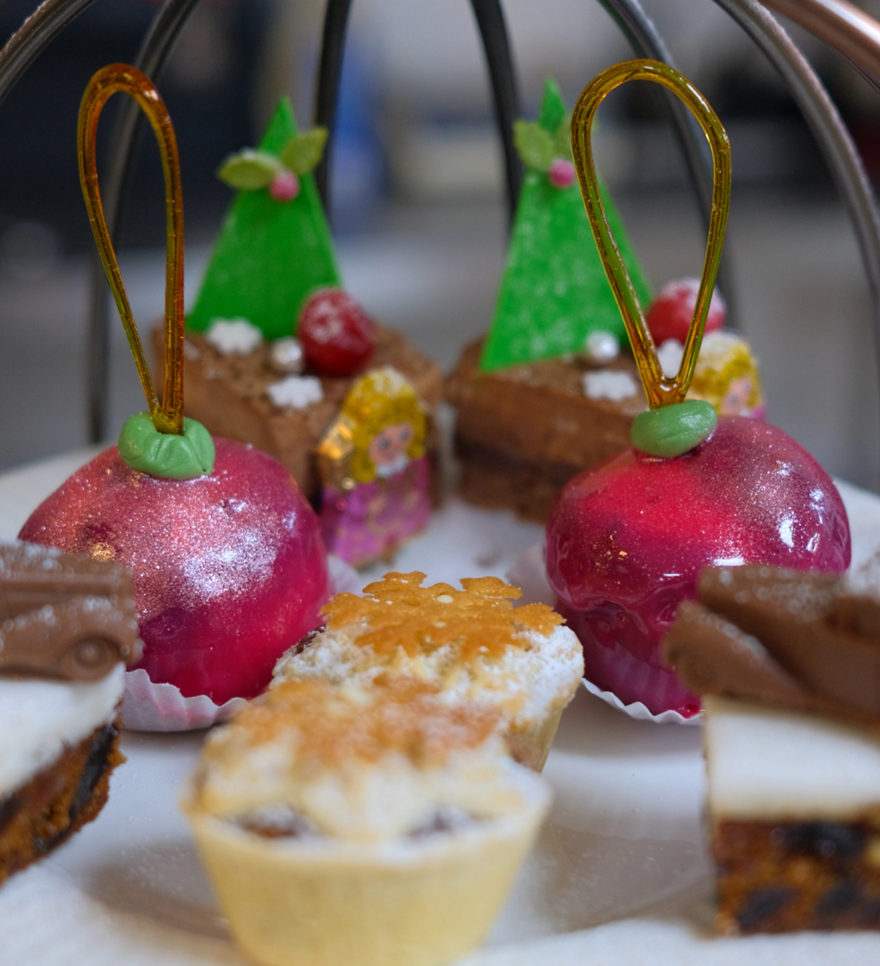 A plate of assorted festive pastries and mini cakes, including red glittery domes, green tree-shaped desserts, and decorated tarts.
