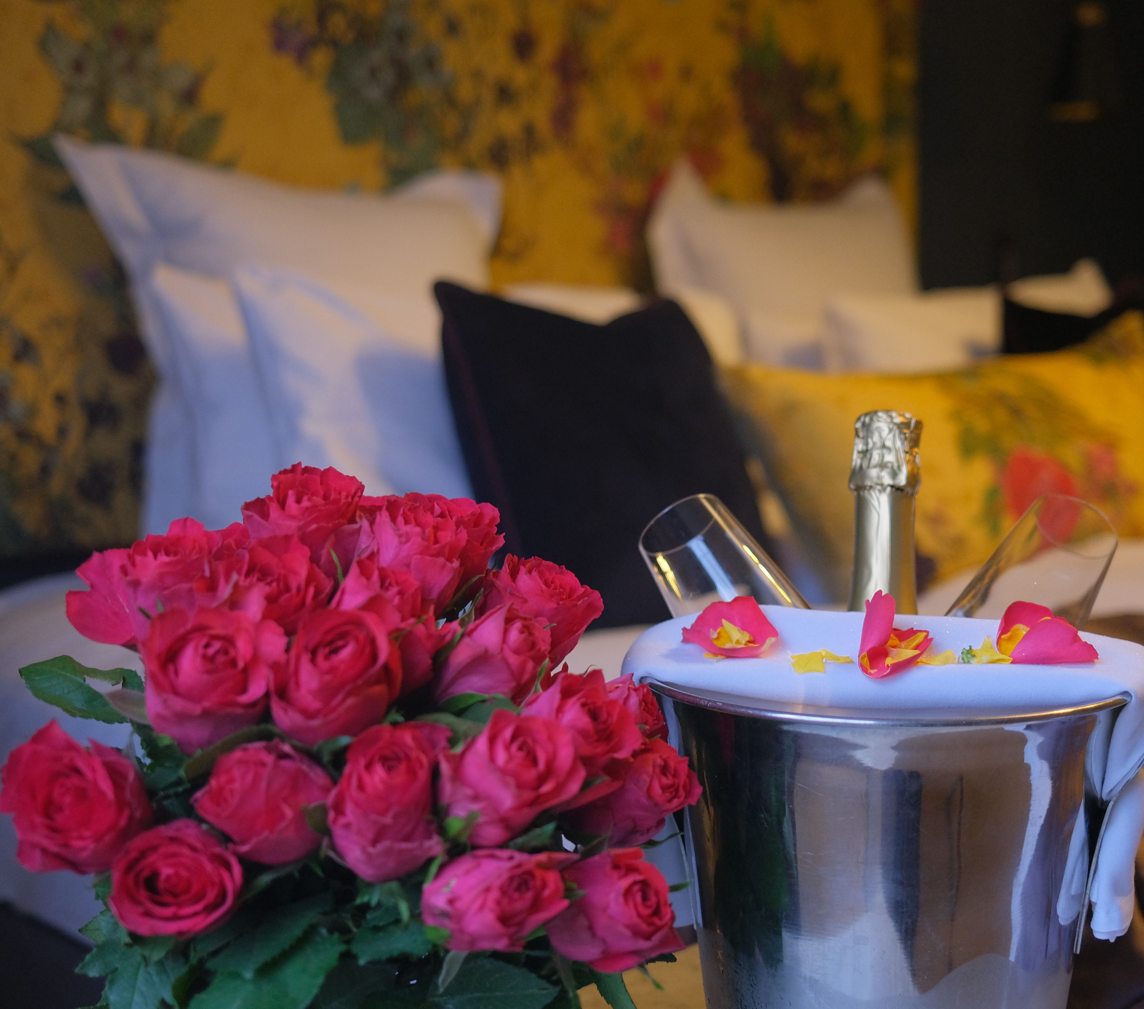 Bouquet of red roses and a champagne bottle in an ice bucket with glasses on a bed in a romantic hotel room