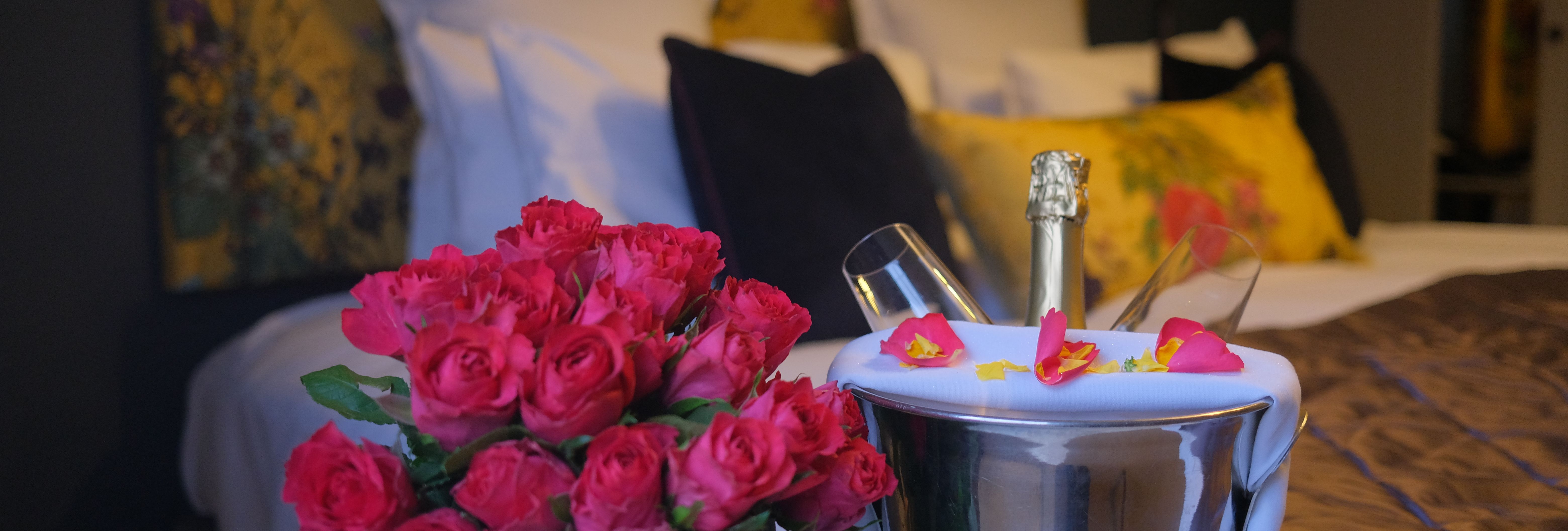 Bouquet of red roses and a champagne bottle in an ice bucket with glasses on a bed in a romantic hotel room