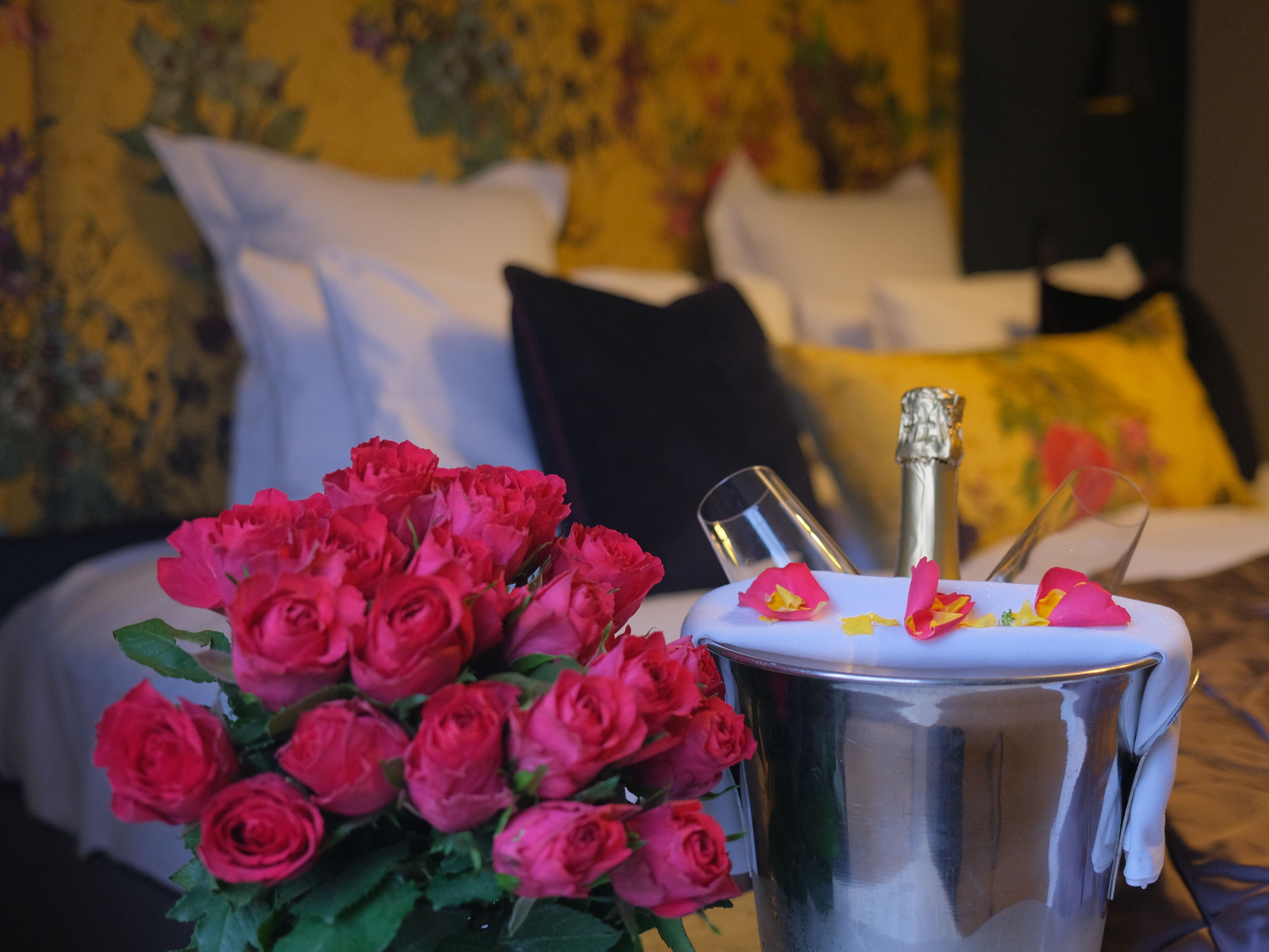 Bouquet of red roses and a champagne bottle in an ice bucket with glasses on a bed in a romantic hotel room