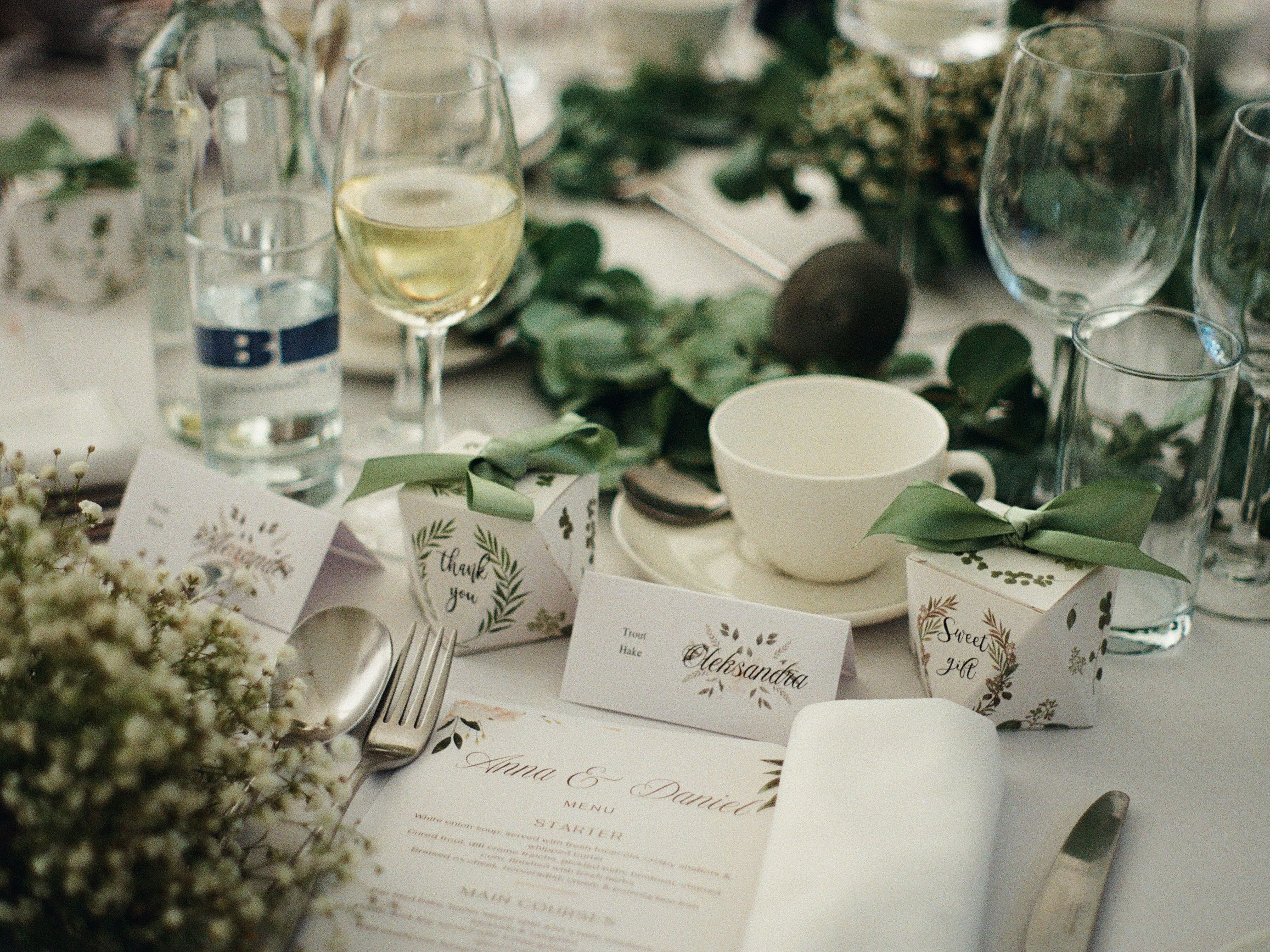 Elegant wedding table setting with glassware, greenery, gifts, and name cards.