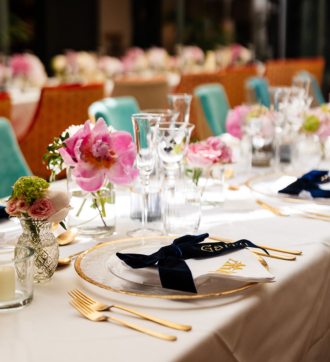 Elegant table setting with pink flowers, glassware, gold cutlery, and personalized napkin at a formal event or wedding reception.