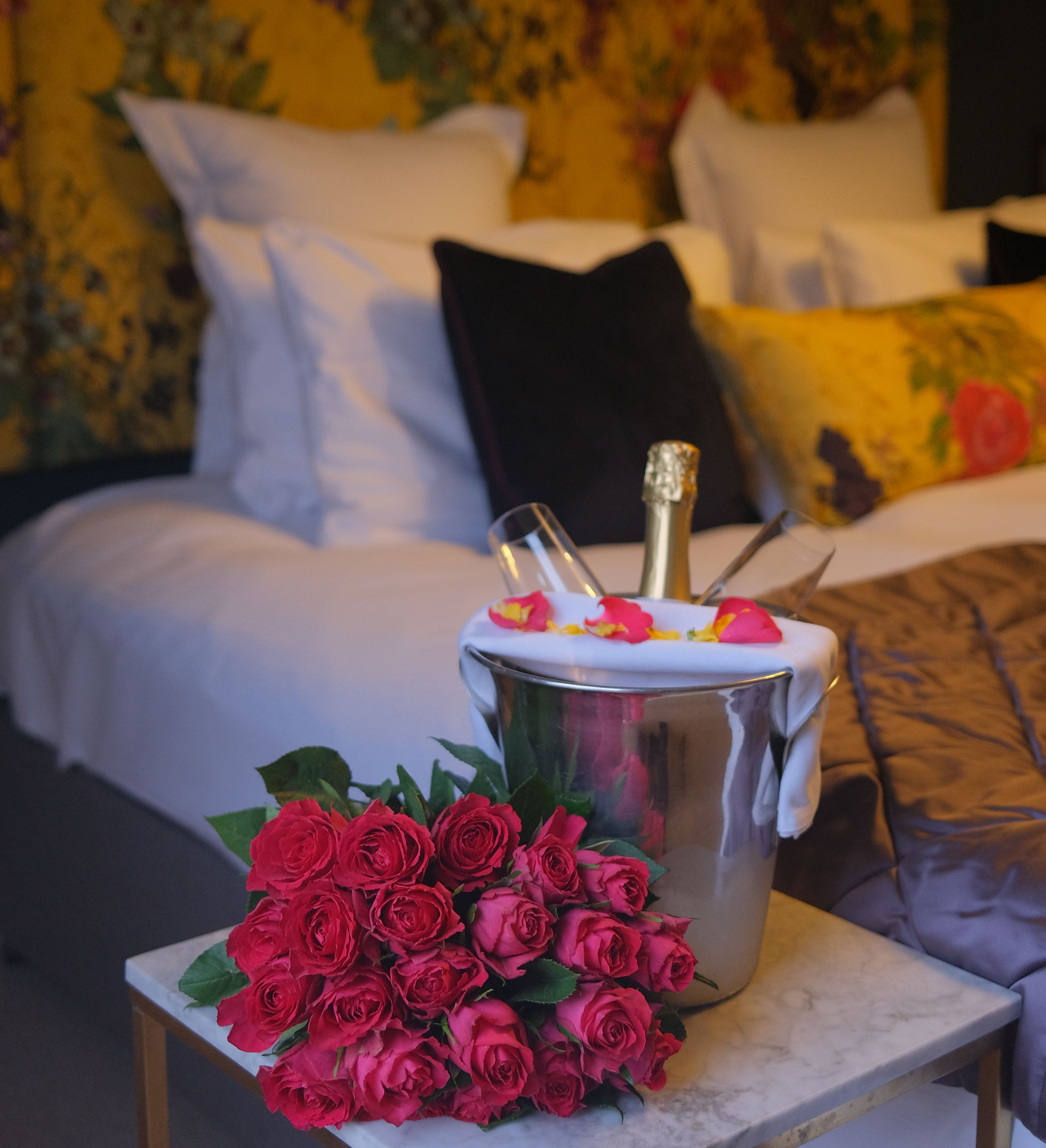 Romantic hotel room with bouquet of red roses and champagne on bedside table