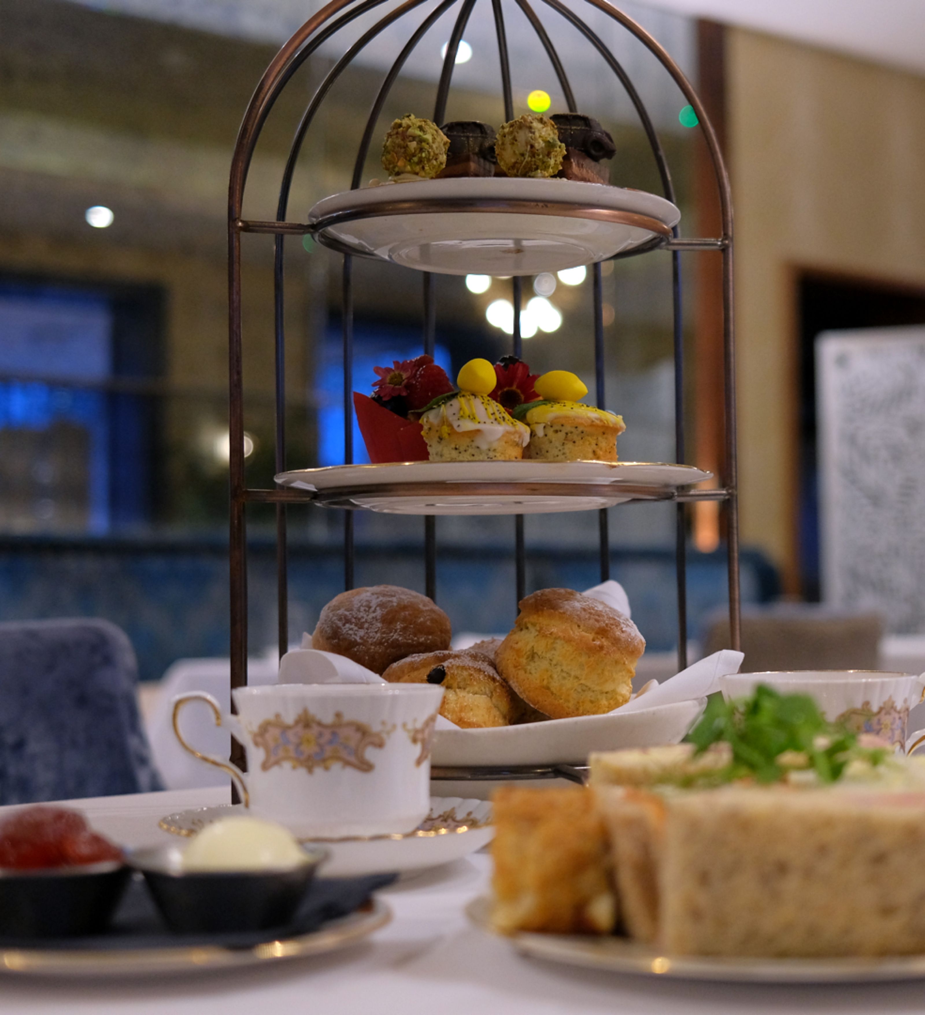 Three-tiered afternoon tea stand with assorted pastries, sandwiches, and scones in an elegant restaurant setting.