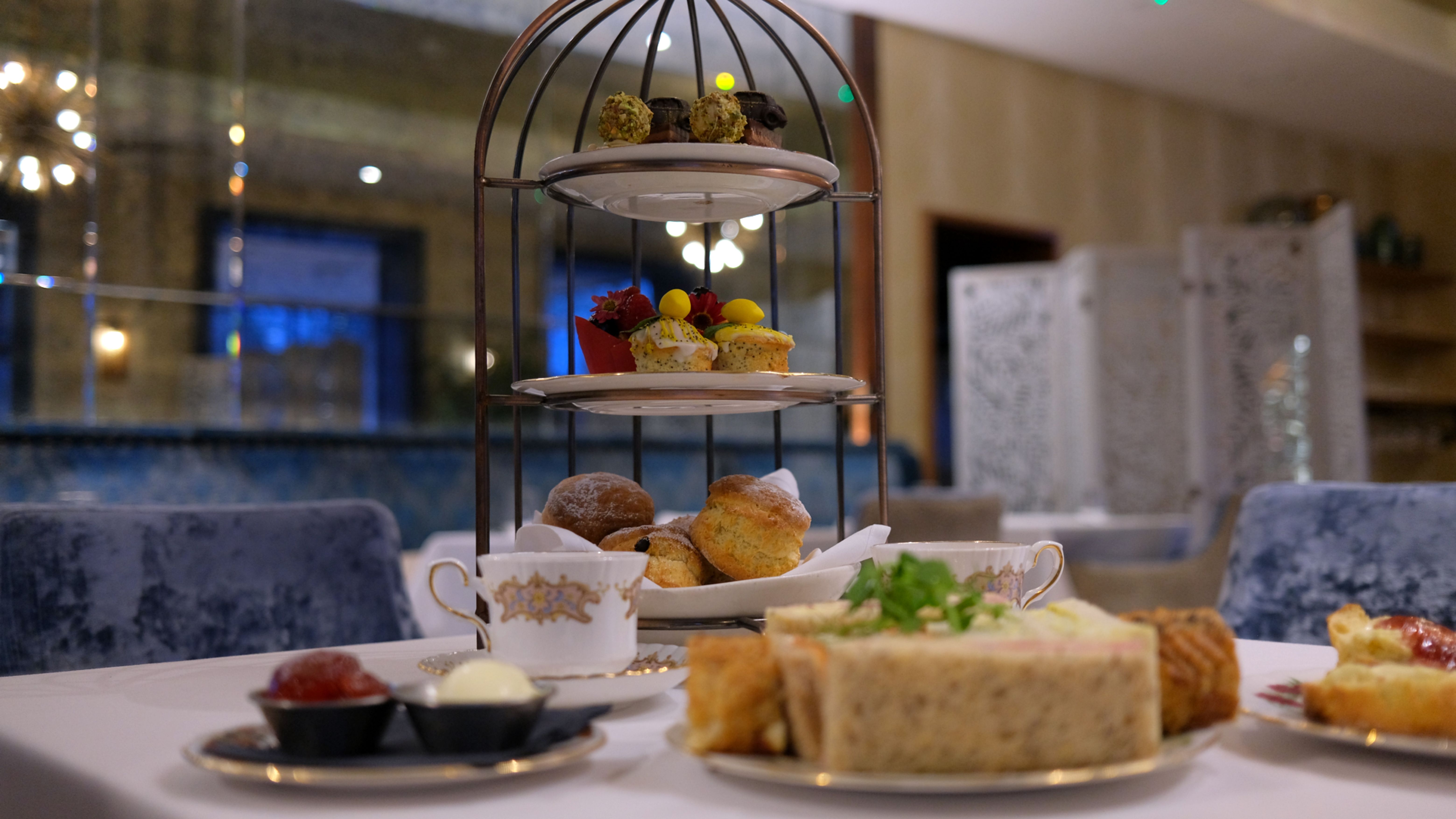 Three-tiered afternoon tea stand with assorted pastries, sandwiches, and scones in an elegant restaurant setting.