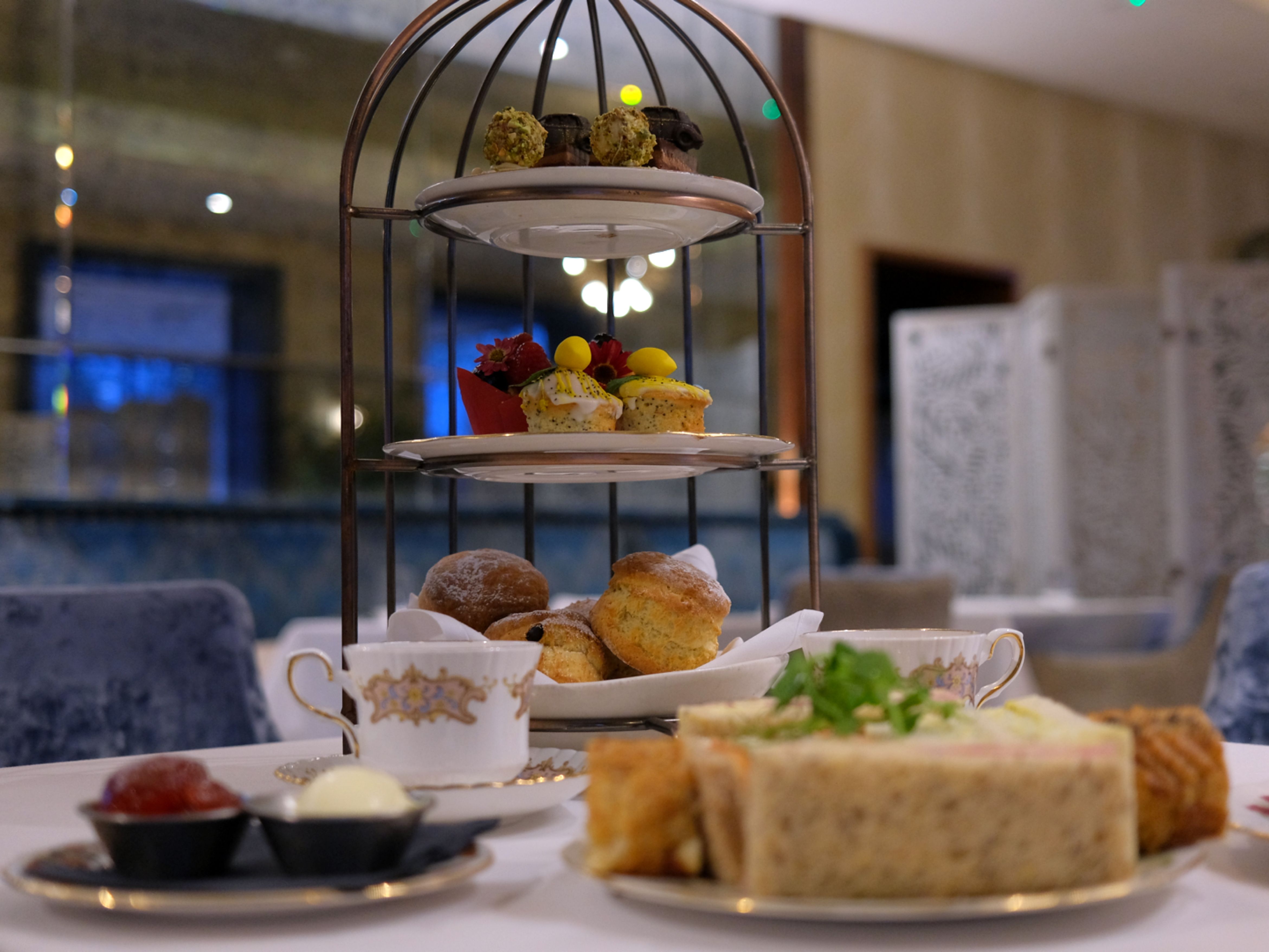 Three-tiered afternoon tea stand with assorted pastries, sandwiches, and scones in an elegant restaurant setting.