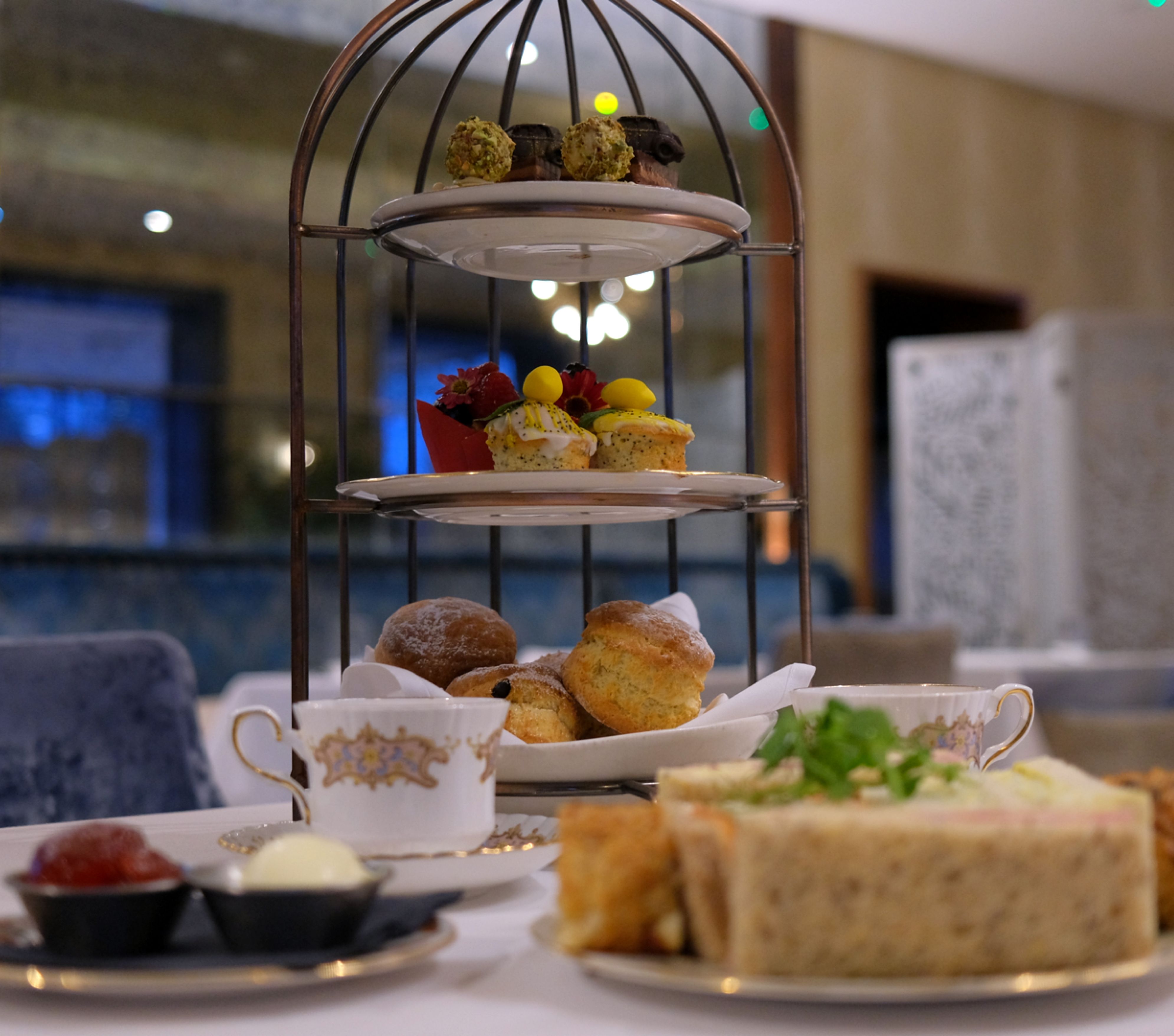 Three-tiered afternoon tea stand with assorted pastries, sandwiches, and scones in an elegant restaurant setting.
