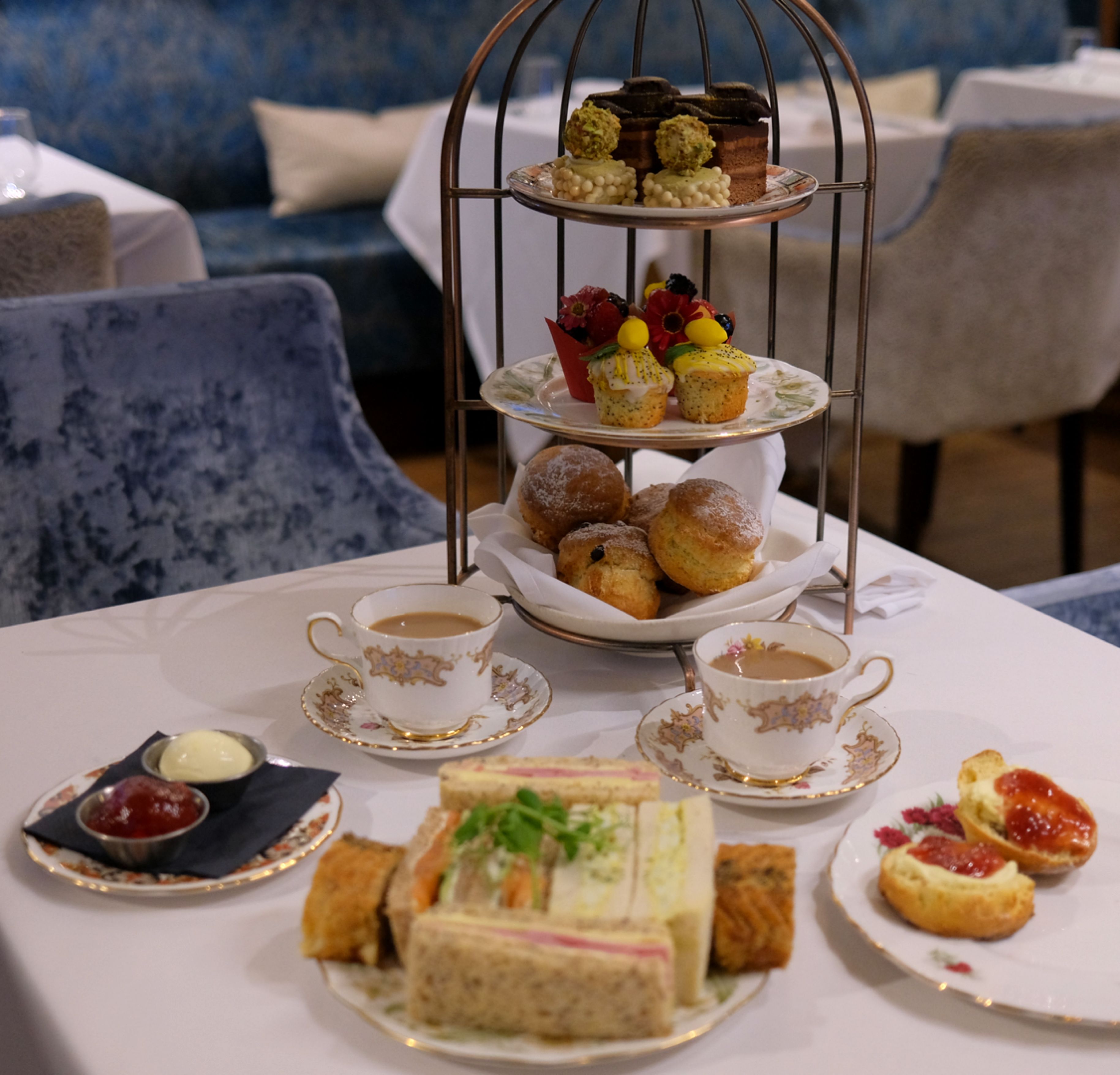 Elegant afternoon tea setup with sandwiches, scones, pastries, and tea on a white tablecloth in a restaurant
