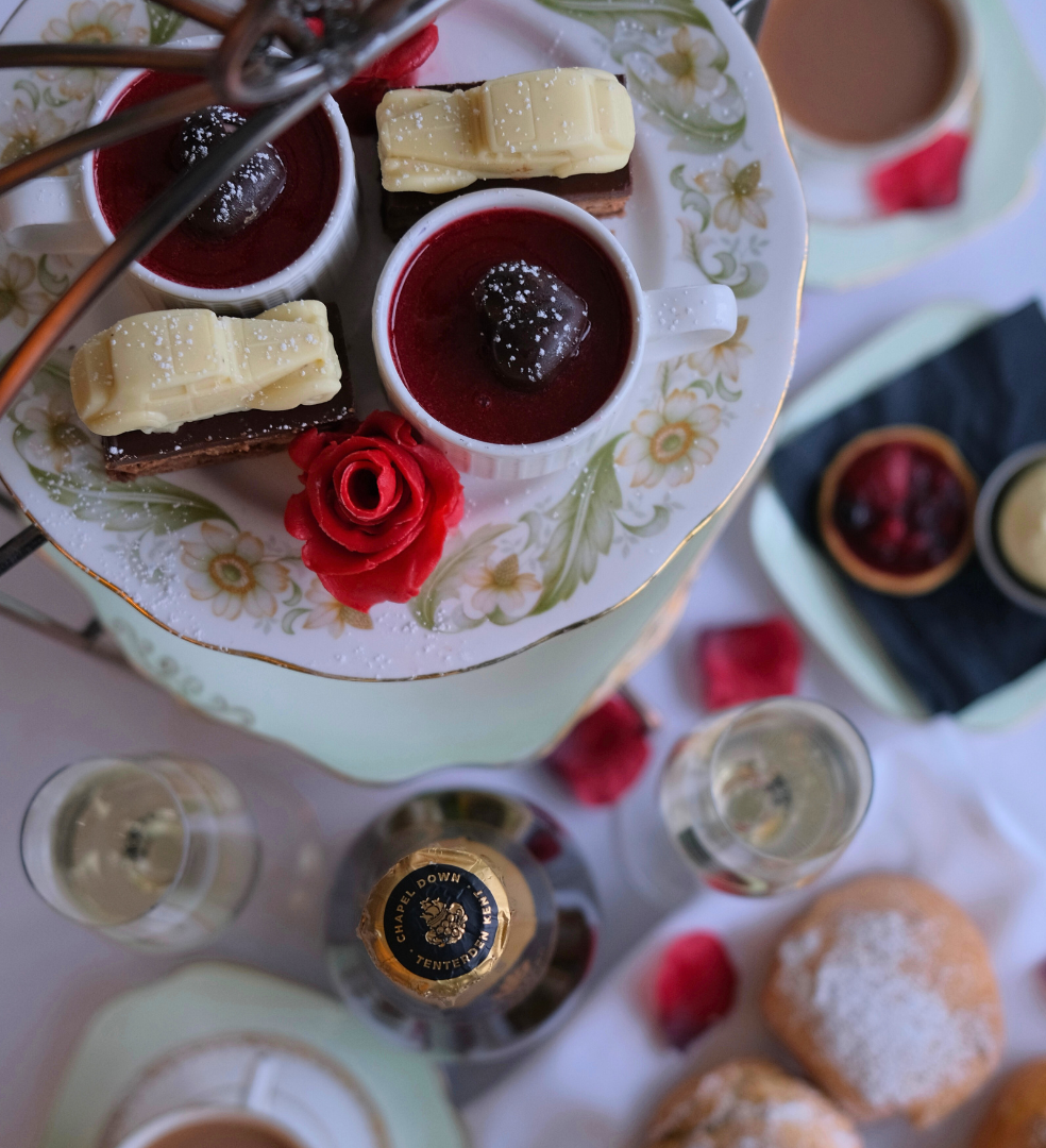 Afternoon tea stand with red berry desserts, white chocolate slices and a sugar rose on a floral plate