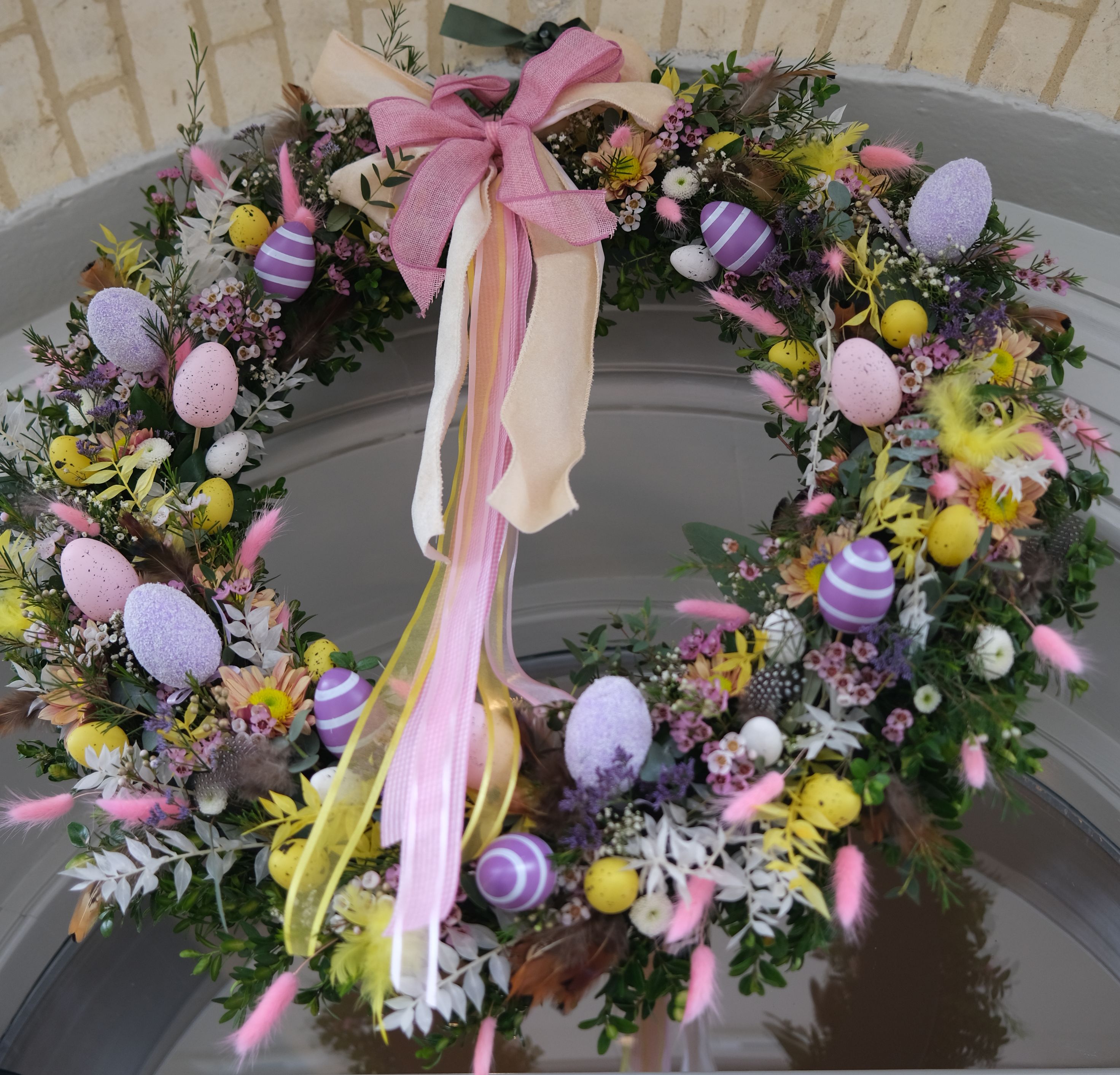 Easter wreath with pastel eggs, flowers and pink ribbon bow on a front door