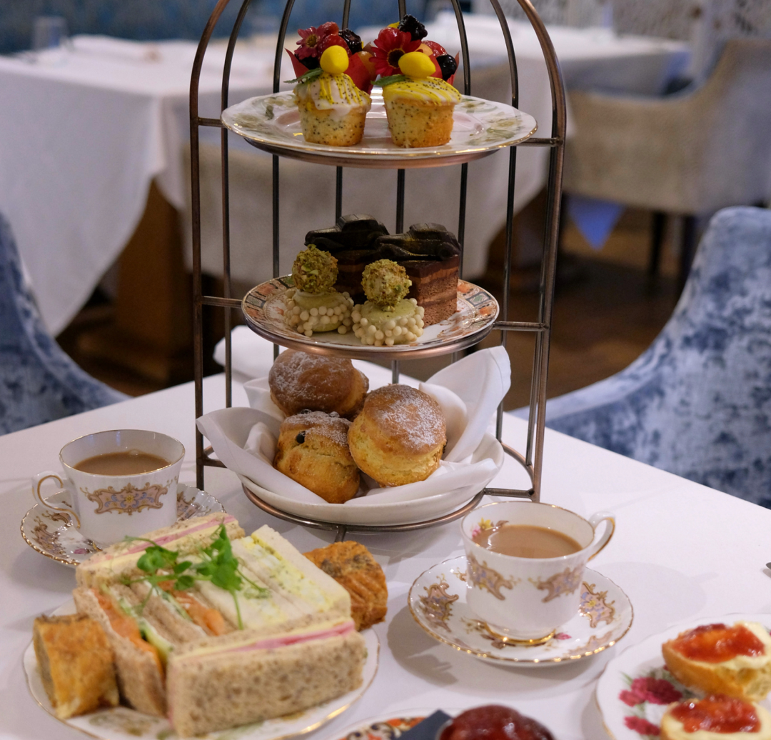 Afternoon tea stand with cakes, scones, sandwiches and two cups of tea on a white table.
