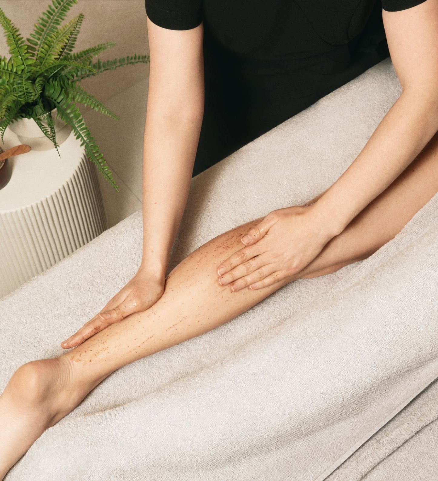 Therapist exfoliating a client’s leg with body scrub on a massage table
