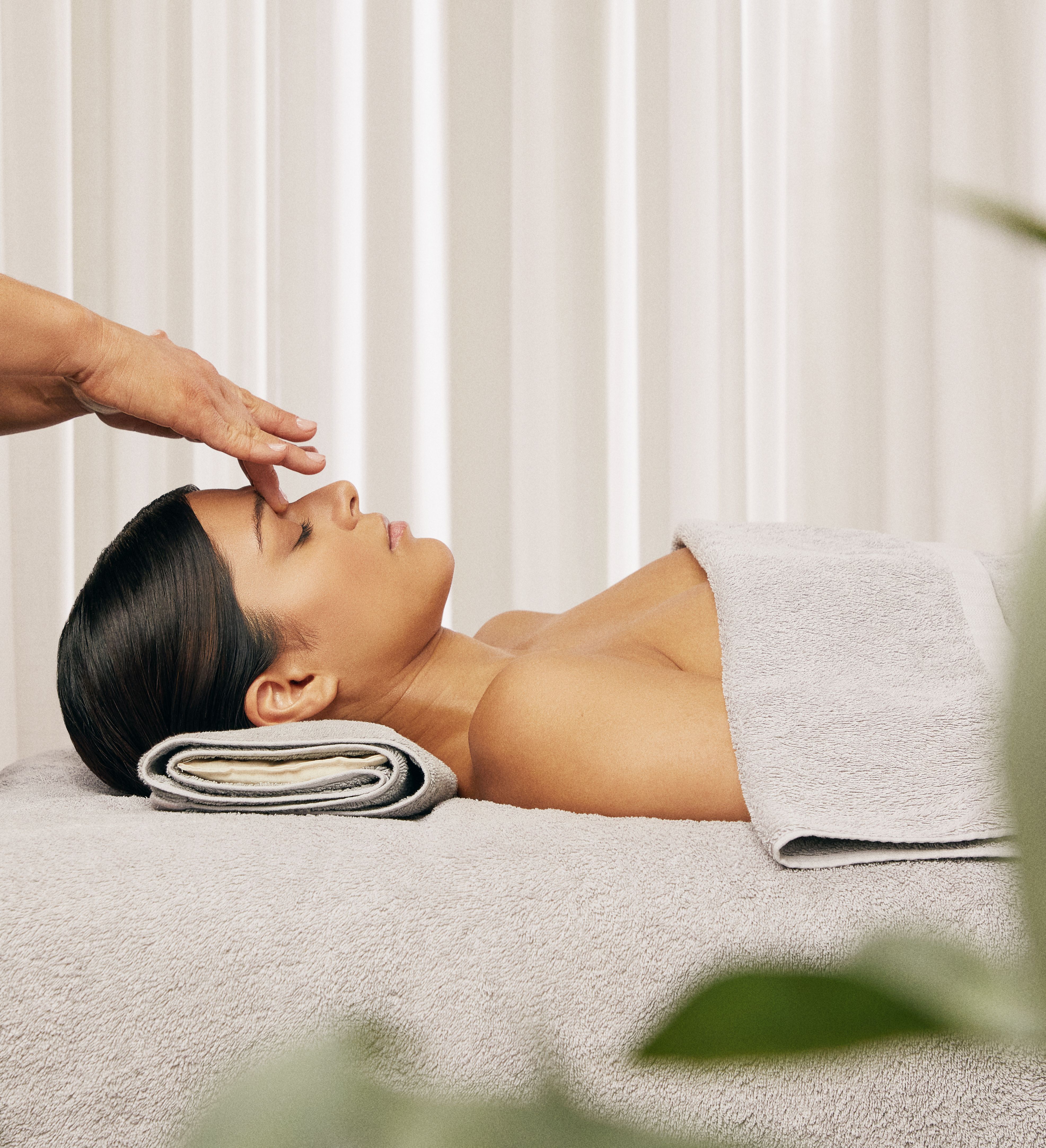 Beautician performing a relaxing facial treatment on a client lying on a spa bed with towels