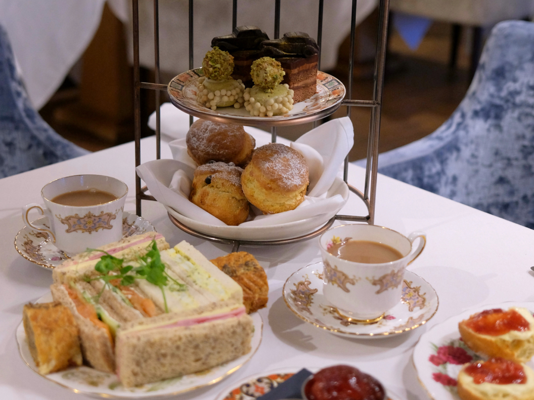 Three-tier afternoon tea stand with cakes, scones, sandwiches and teacups on a white table
