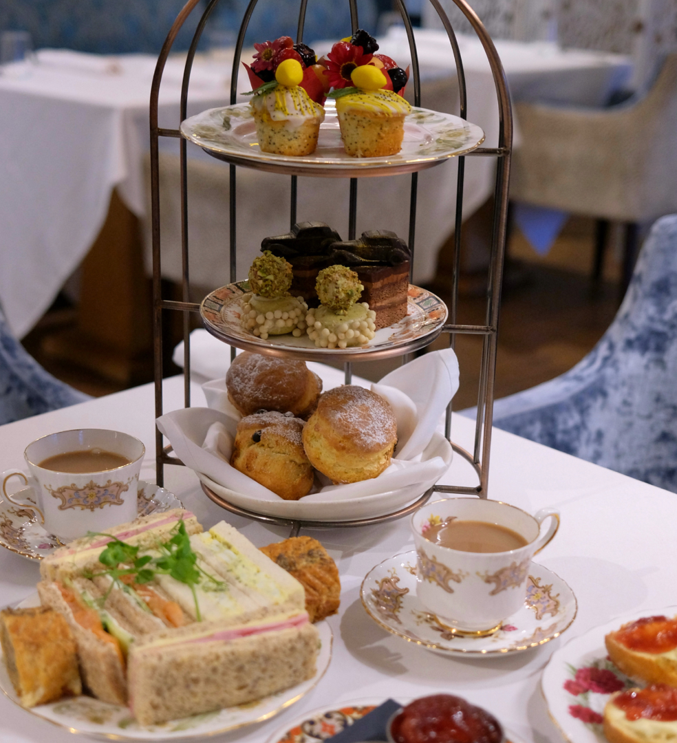 Three-tier afternoon tea stand with cakes, scones, sandwiches and teacups on a white table