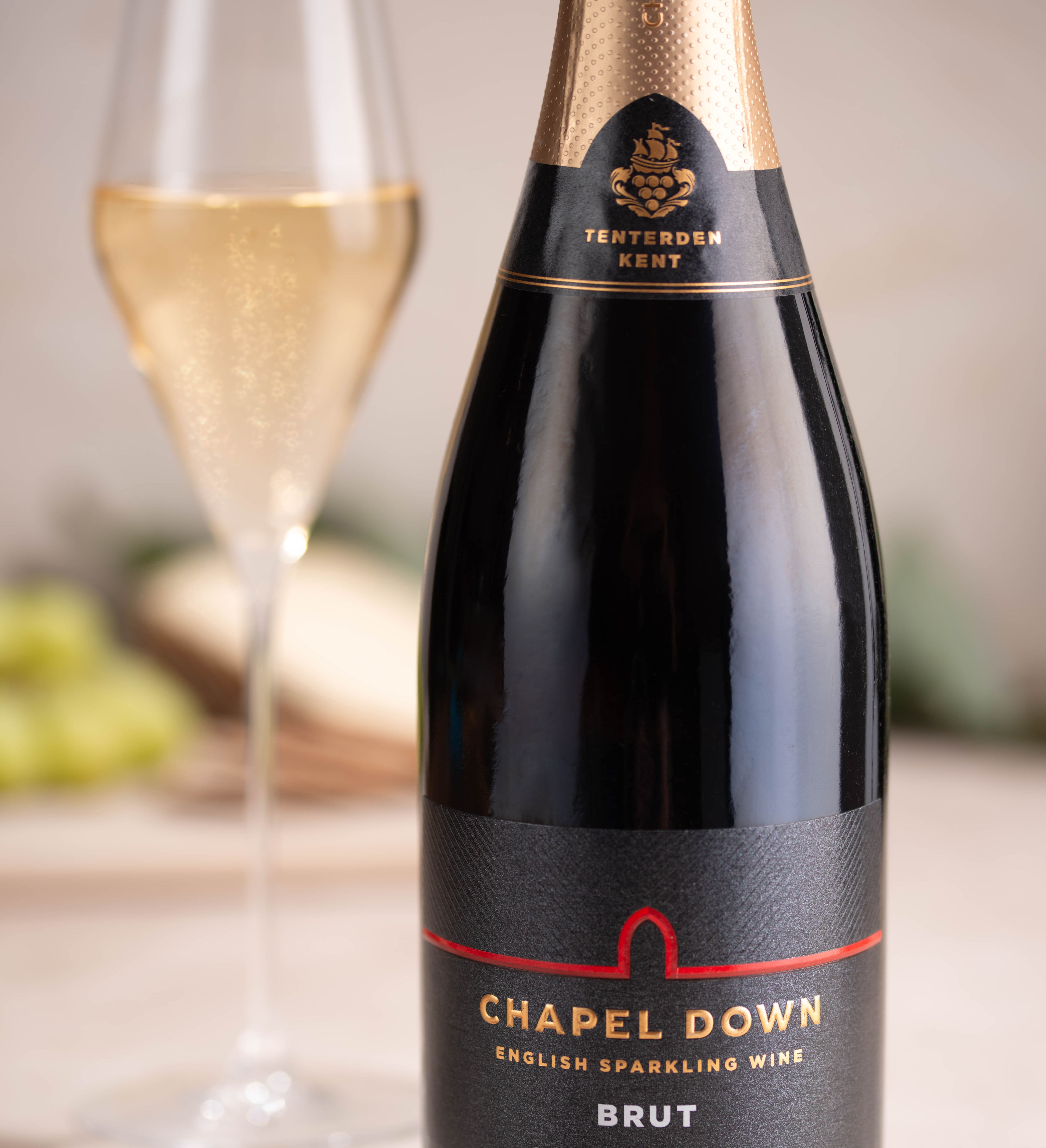 Close-up of a Chapel Down Brut English sparkling wine bottle with a glass of fizz in the background
