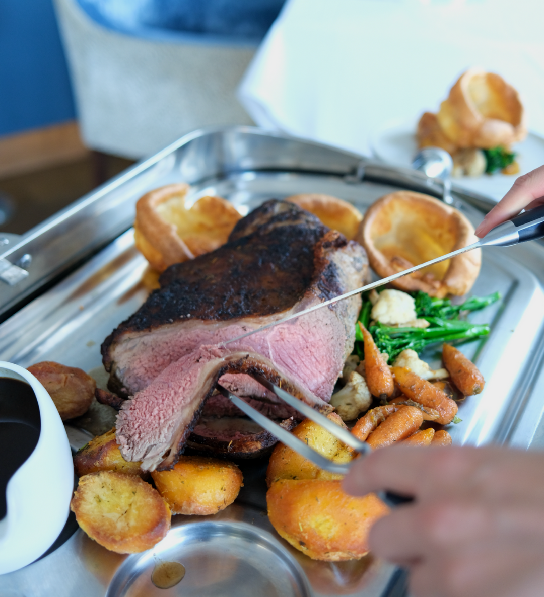 Carving roast beef with Yorkshire puddings, roast potatoes and vegetables on a serving tray