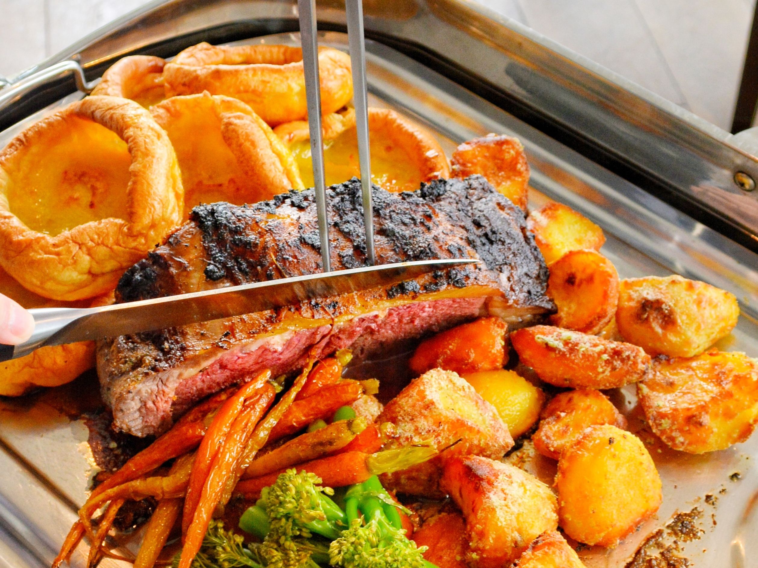 Carving a Sunday roast of beef with Yorkshire puddings, roast potatoes and vegetables on a serving tray