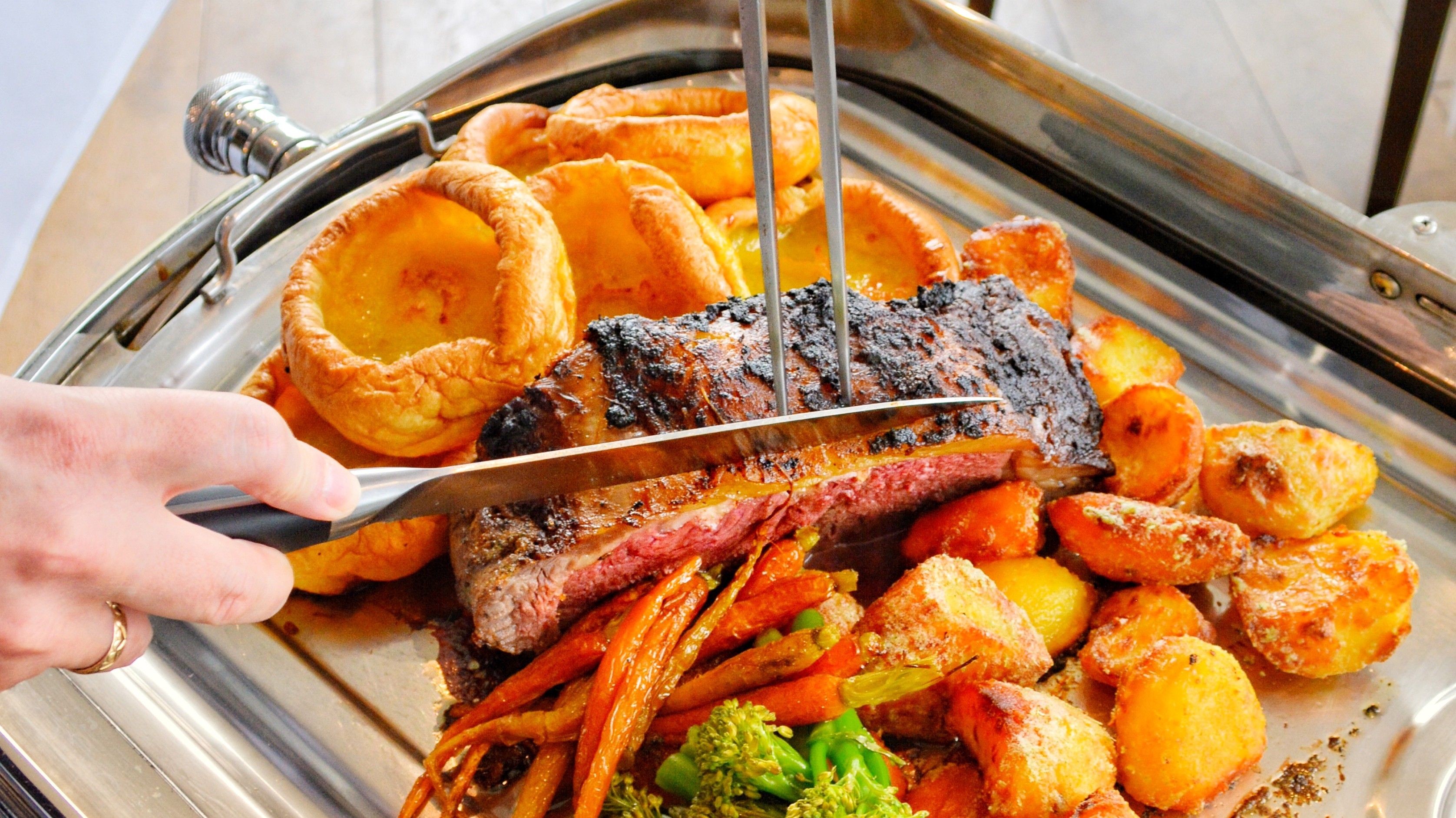Carving a Sunday roast of beef with Yorkshire puddings, roast potatoes and vegetables on a serving tray