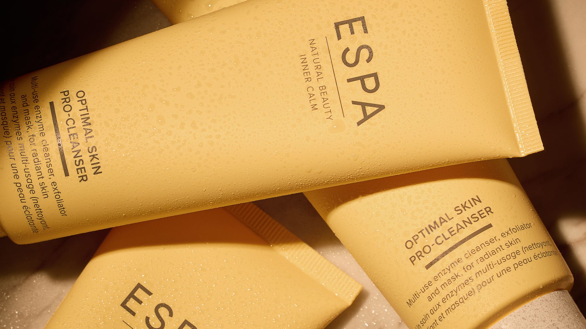 Close-up of ESPA Optimal Skin Pro-Cleanser tubes with water droplets on a stone surface