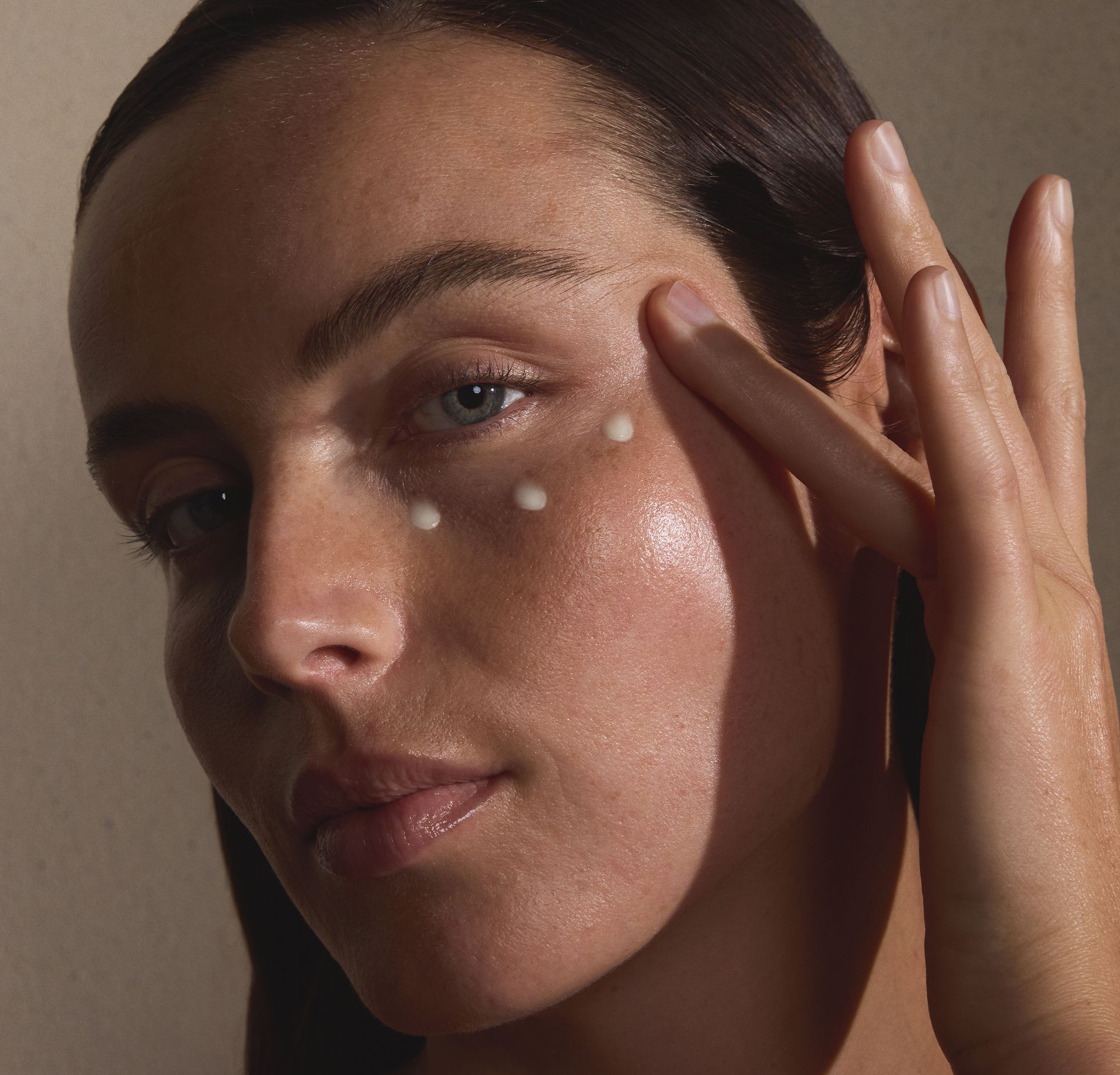 Close-up of a woman applying small dots of face cream to her cheekbone