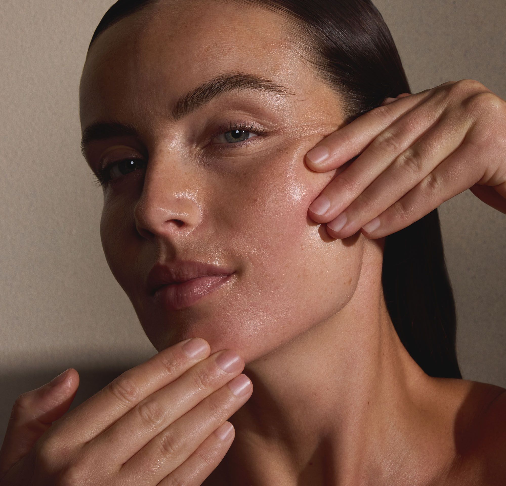 Close-up of a woman touching her cheek with fingertips, showing a natural, dewy complexion.