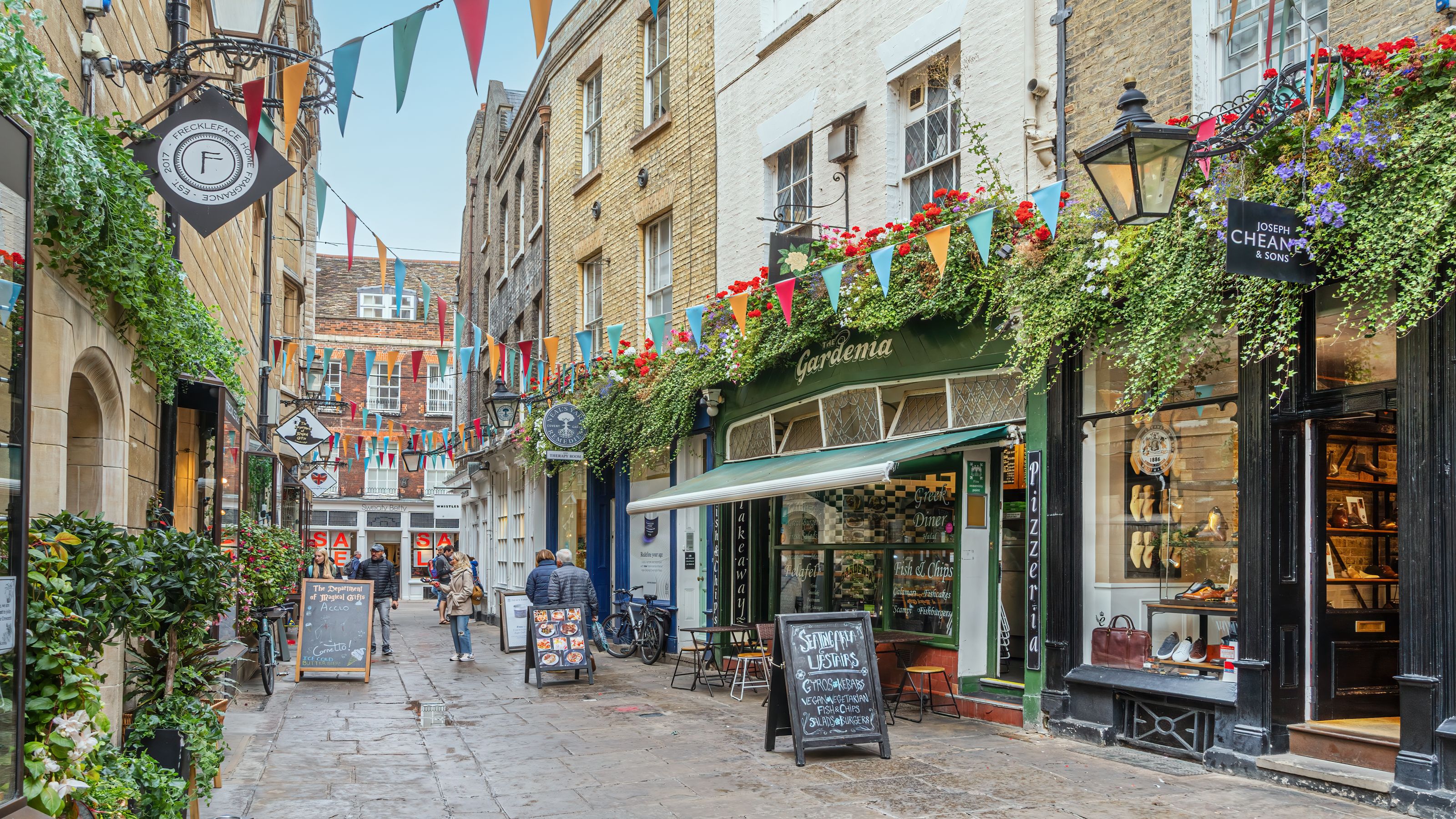 People browsing a flower-filled lane of cafés and boutiques while shopping in Cambridge.