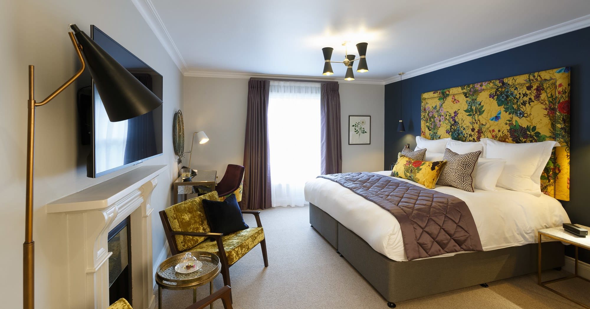 The Rosa feature room at Gonville Hotel in Cambridge, with bold floral décor, plush bedding, velvet chairs, and a cosy, modern design.