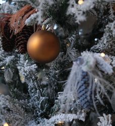 Close-up of a decorated Christmas tree branch with snow, pinecones, and ornaments